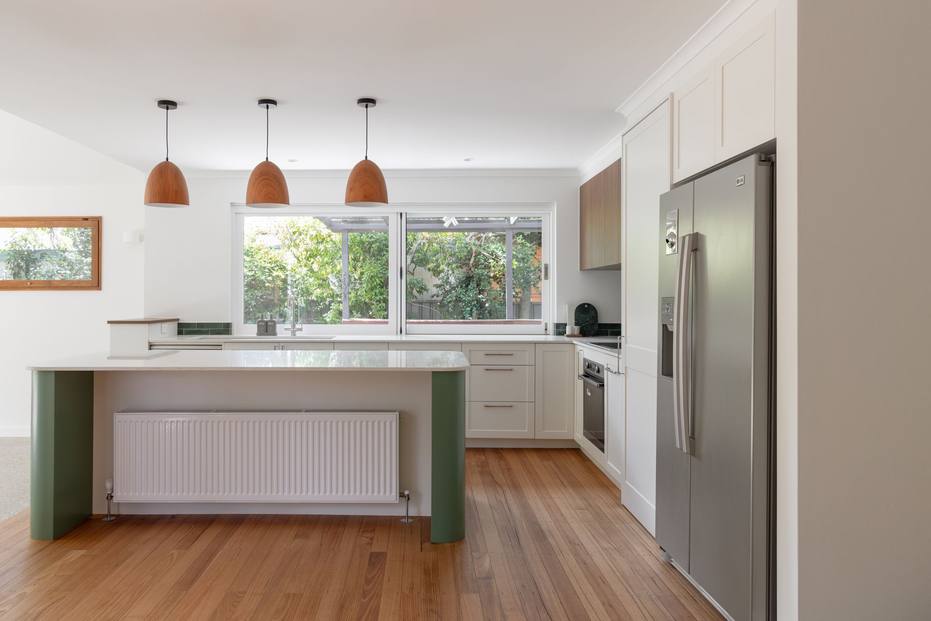 Bright modern kitchen with white cabinets, wood floors, island, stainless fridge, and large window over the sink