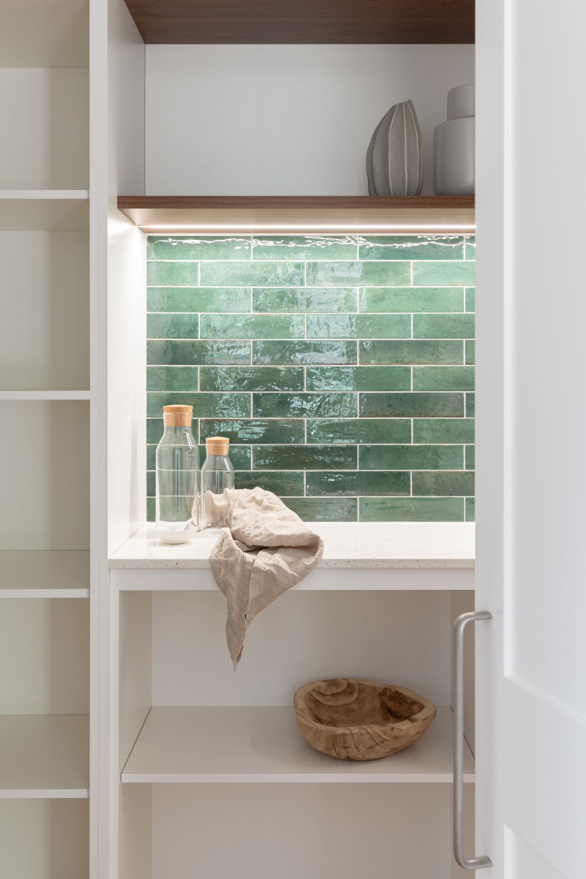 Bathroom nook with green tile backsplash, small shelf, candles, towel, and woven basket.