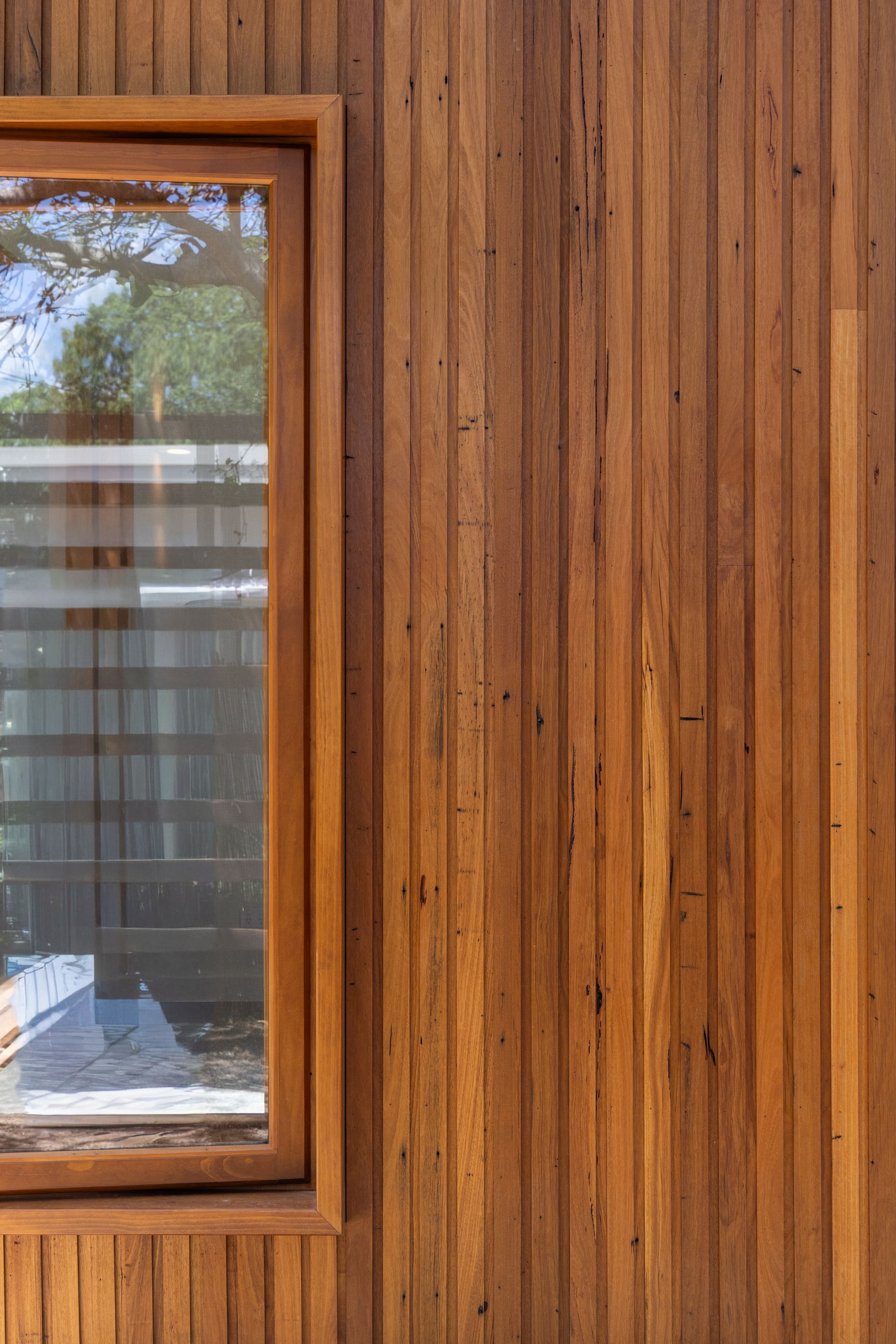 Wood-paneled wall with a small window reflecting trees and sky