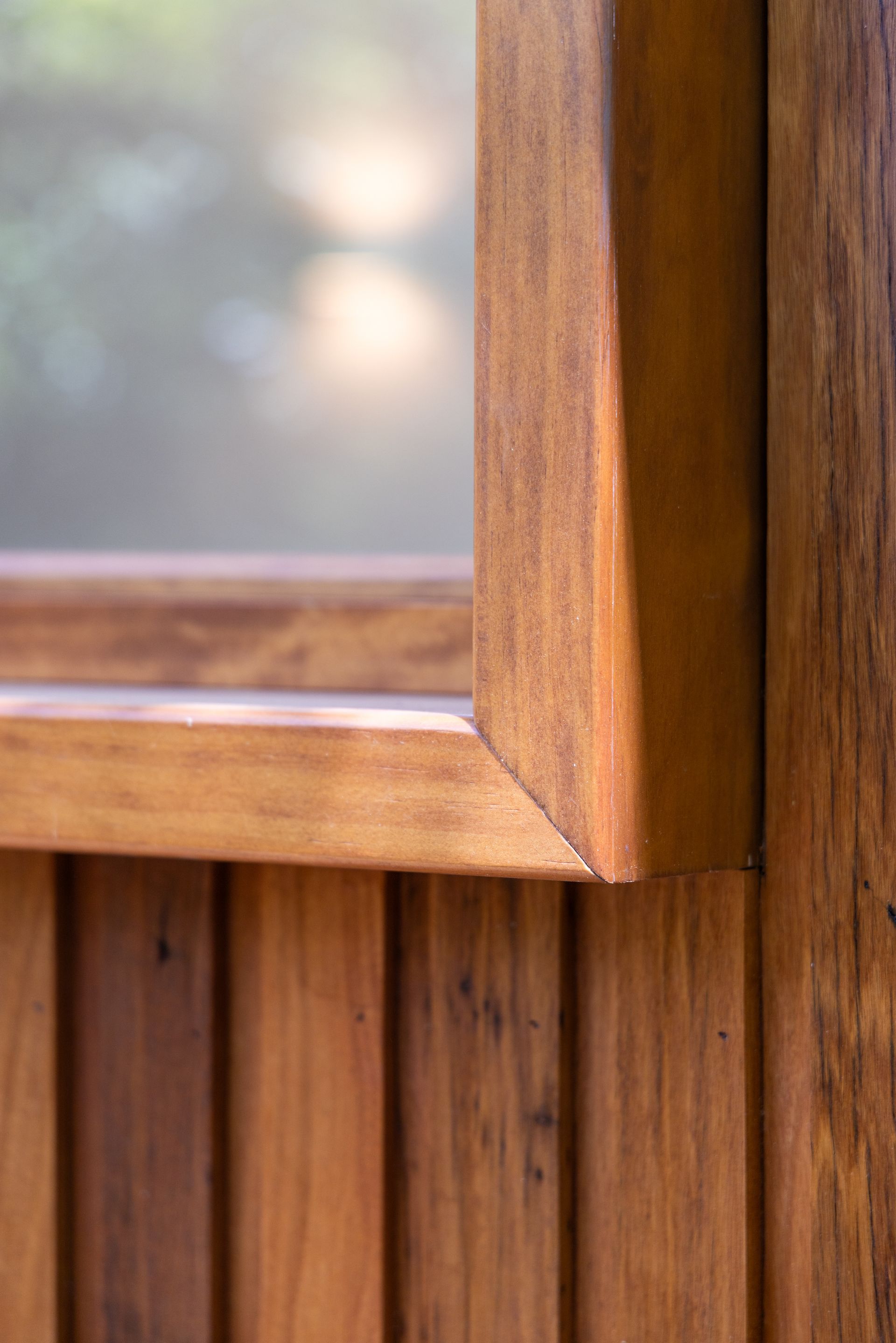 Close-up of a wooden window frame and frosted glass on a vertical wood-paneled wall