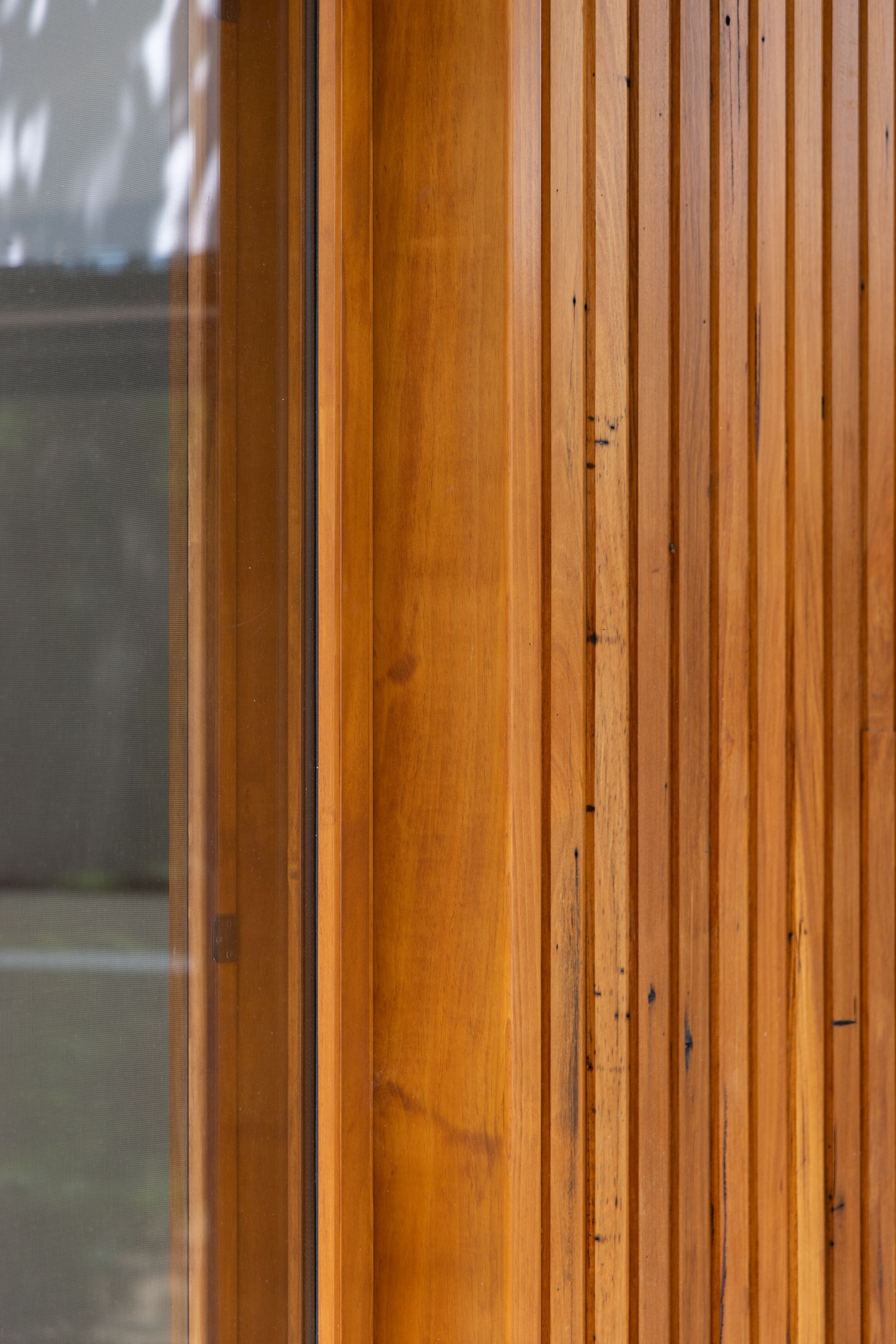 Close-up of a vertical wooden wall panel beside a frosted glass window