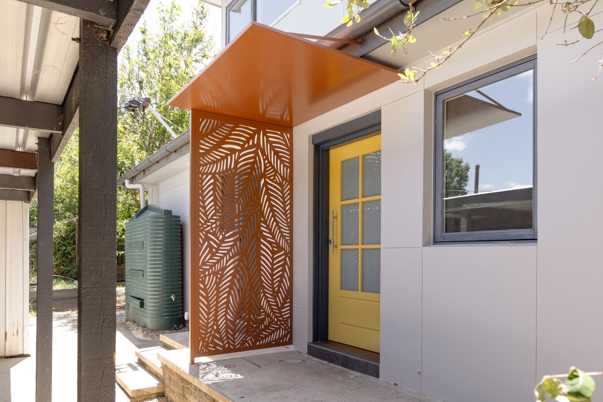 Modern house entrance with a yellow door, orange canopy, and decorative metal privacy screen