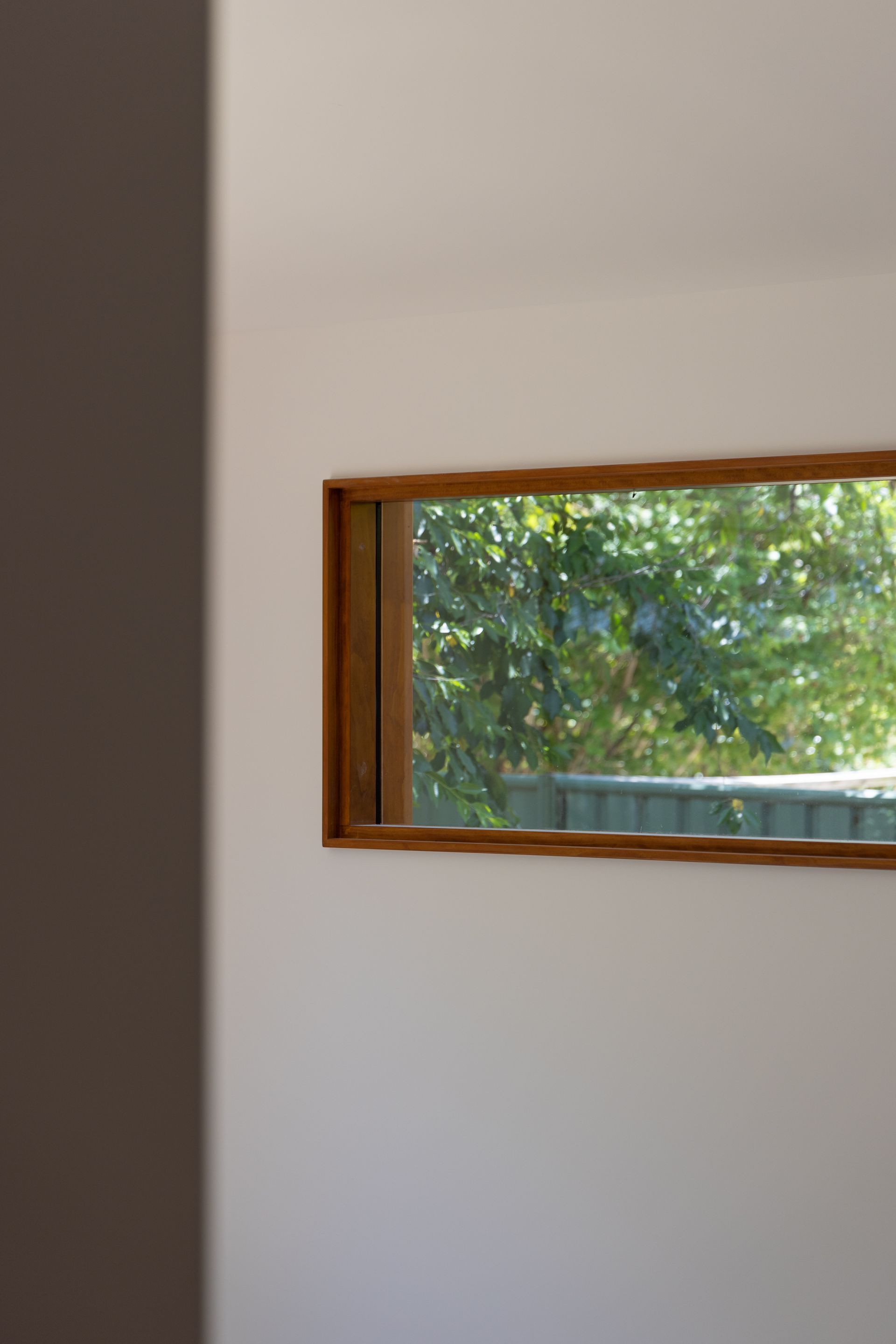 White interior wall with a small wooden-framed window showing green trees outside.