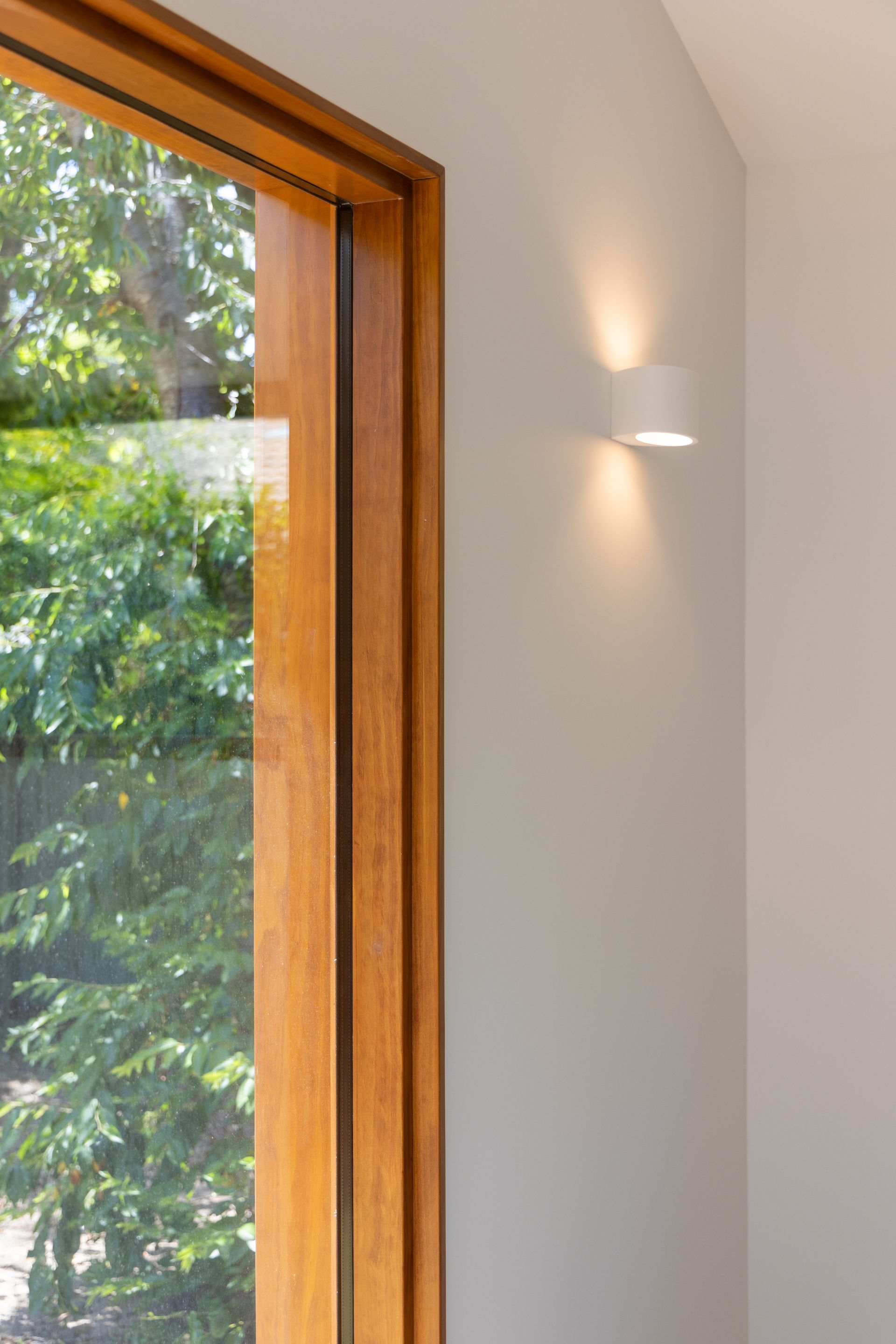 Modern interior wall with a wooden-framed window and a small wall sconce, lit by daylight