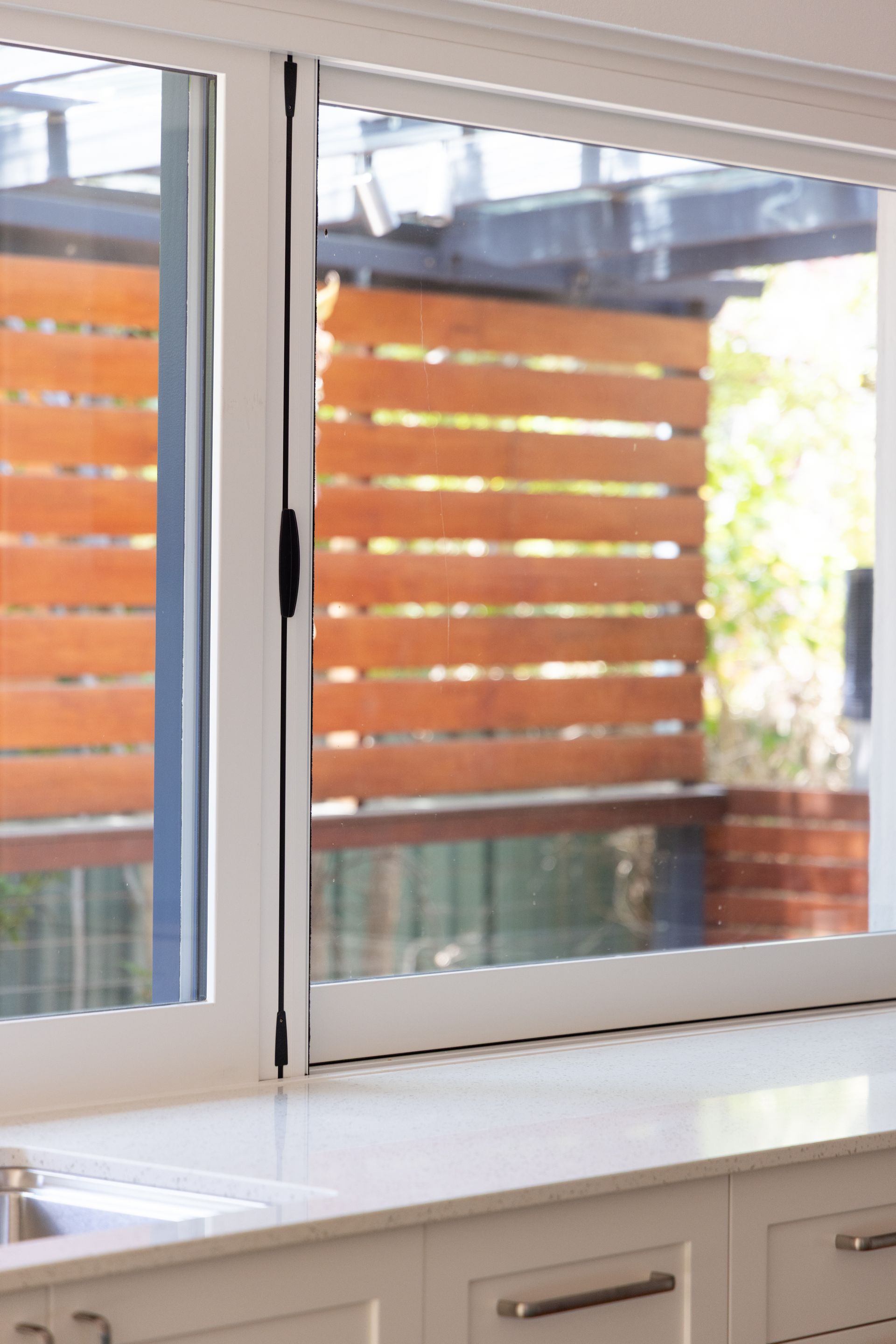 Kitchen window with white frame, sink, and wood privacy slats outside