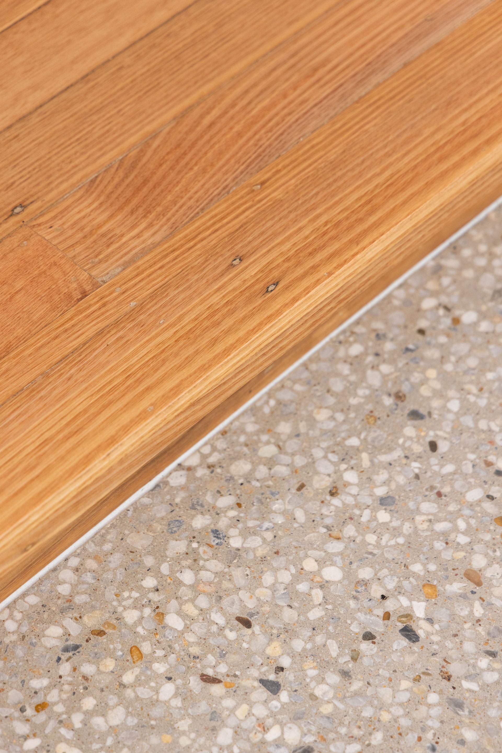 Wooden floor meeting speckled terrazzo tile at a diagonal edge