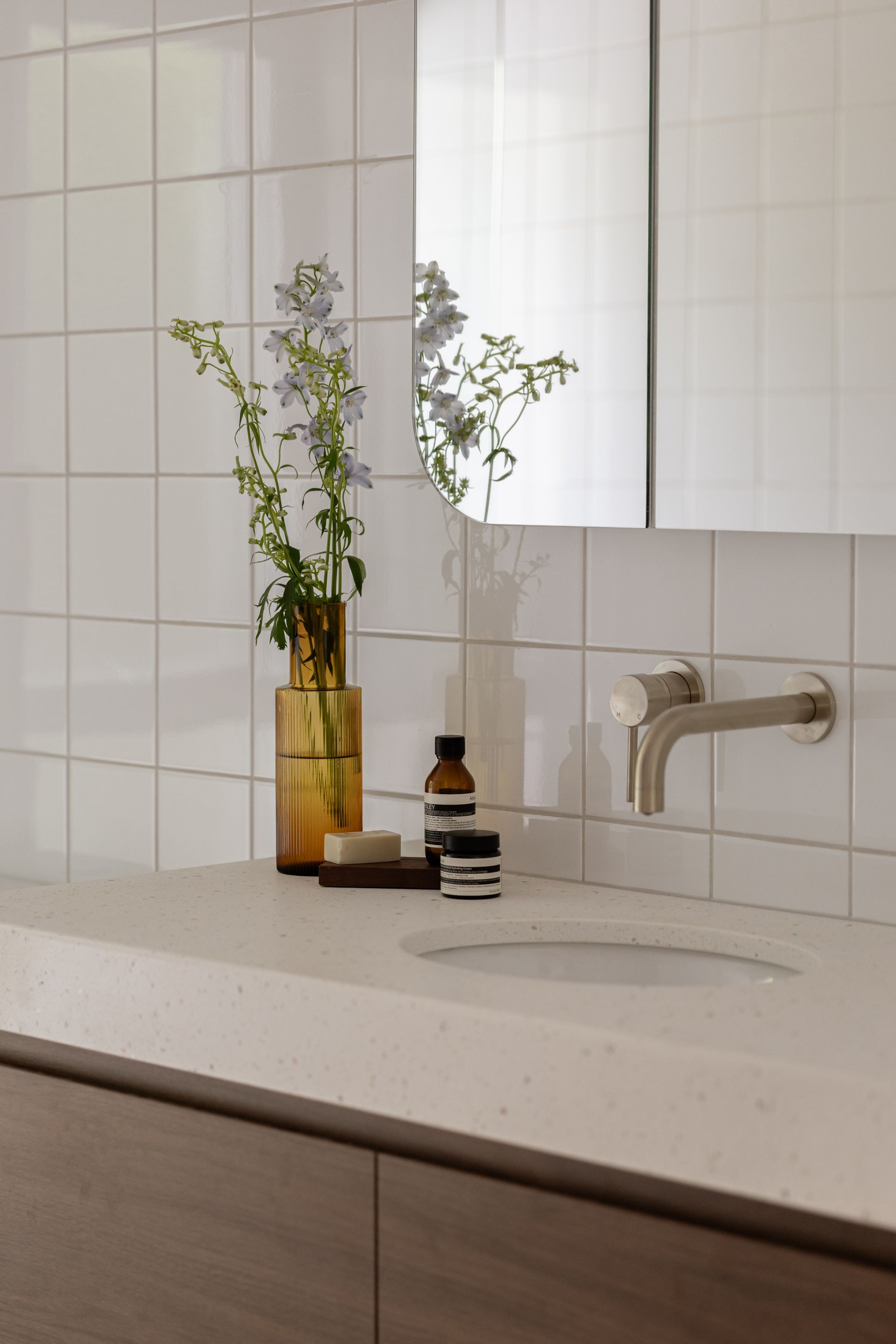 Minimalist bathroom sink with a gold vase, small bottle, mirror, and wall-mounted faucet
