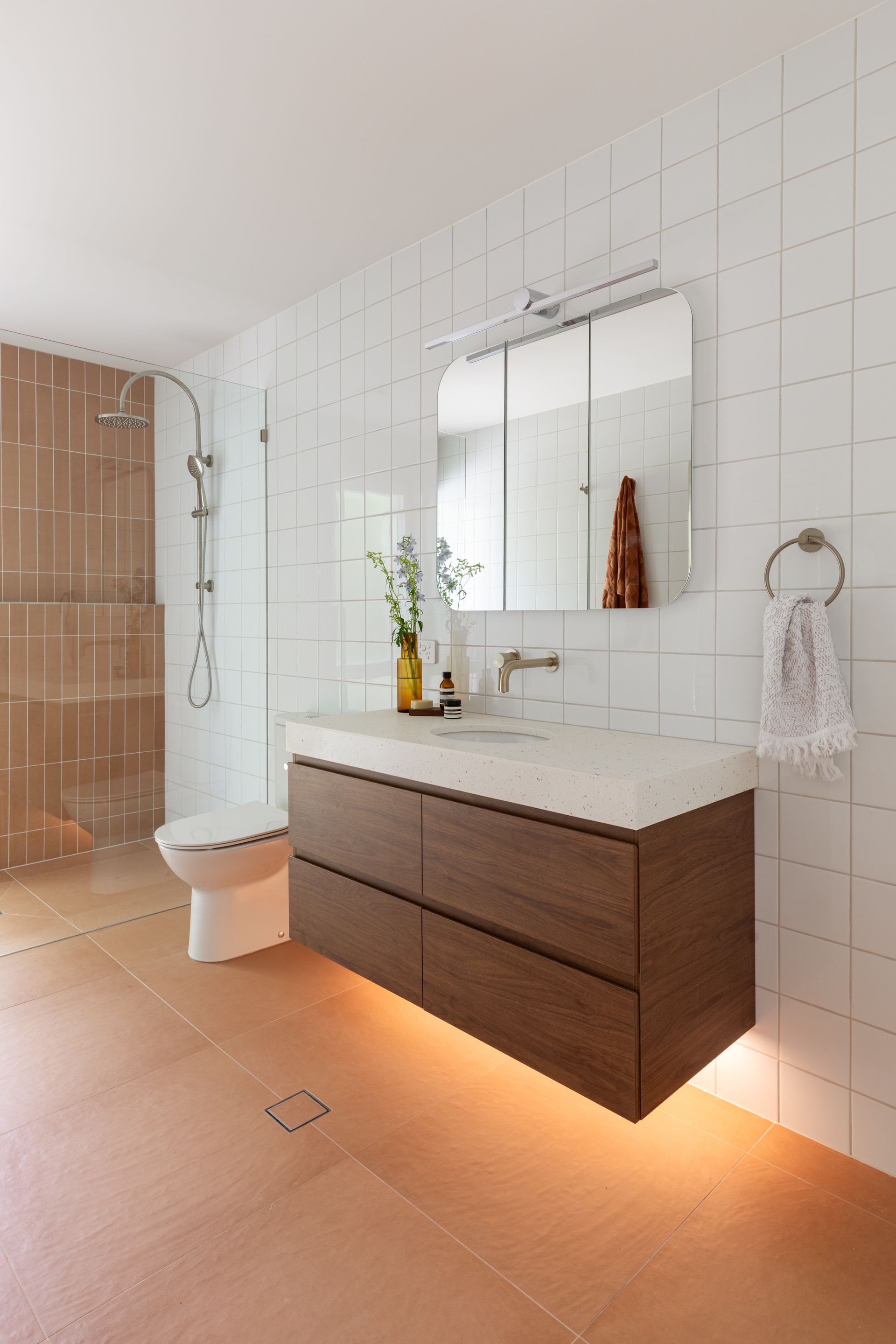 Modern bathroom with floating dark wood vanity, mirror, white tiled walls, toilet, and walk-in shower.