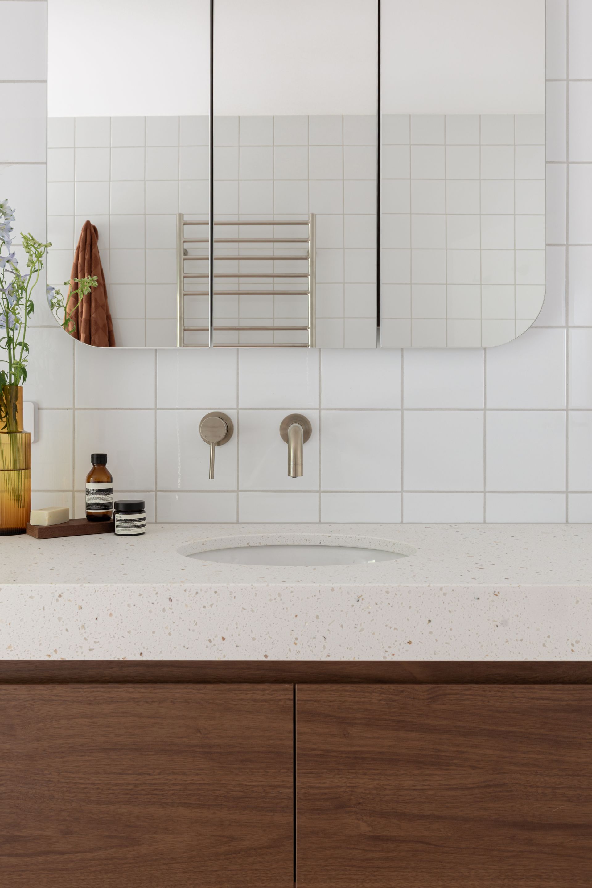 Modern bathroom vanity with wood cabinets, speckled white countertop, round sink, and mirror over white tile wall