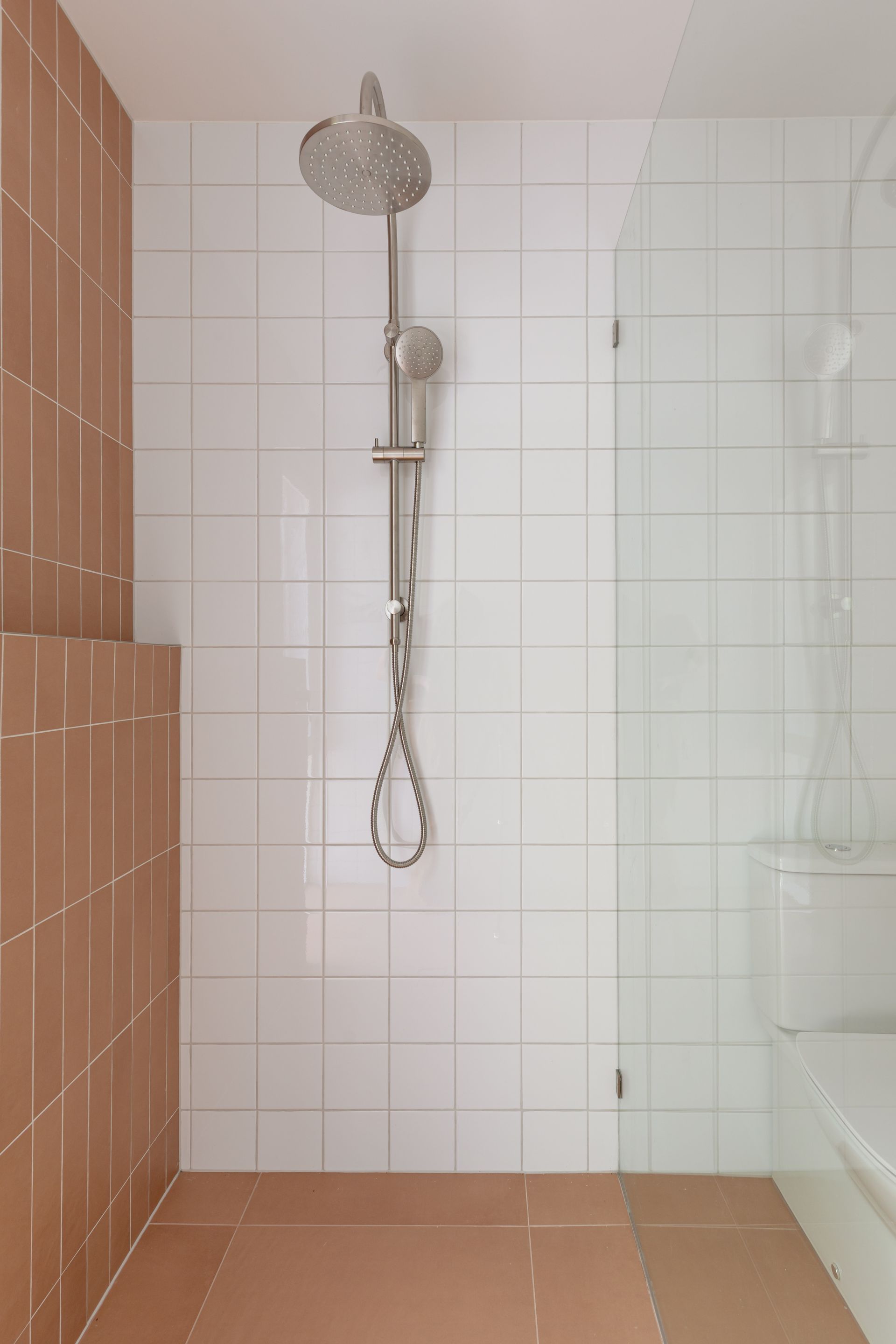 Modern tiled shower stall with chrome rain showerhead and glass partition