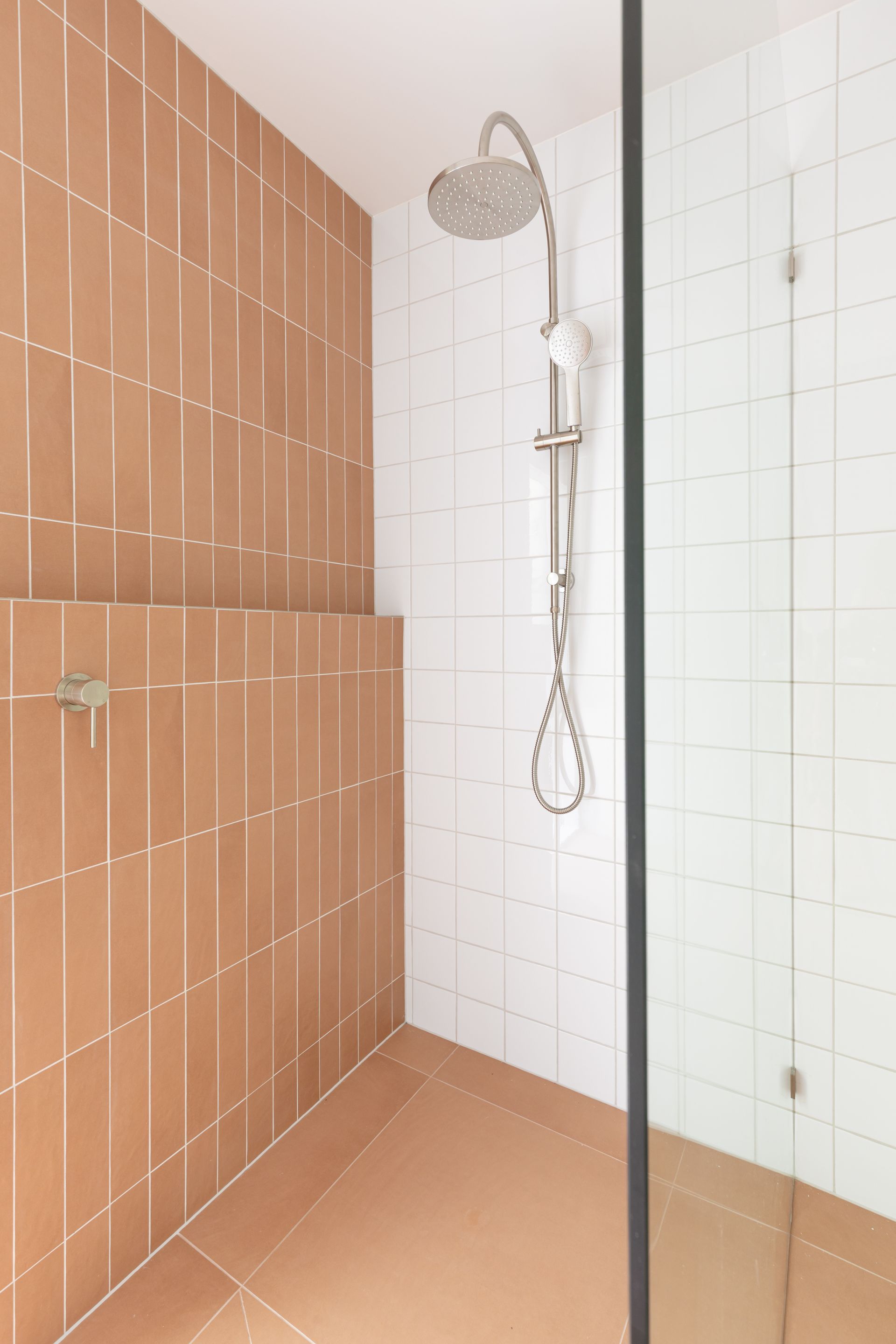 Walk-in shower with terracotta and white tiled walls and a handheld showerhead