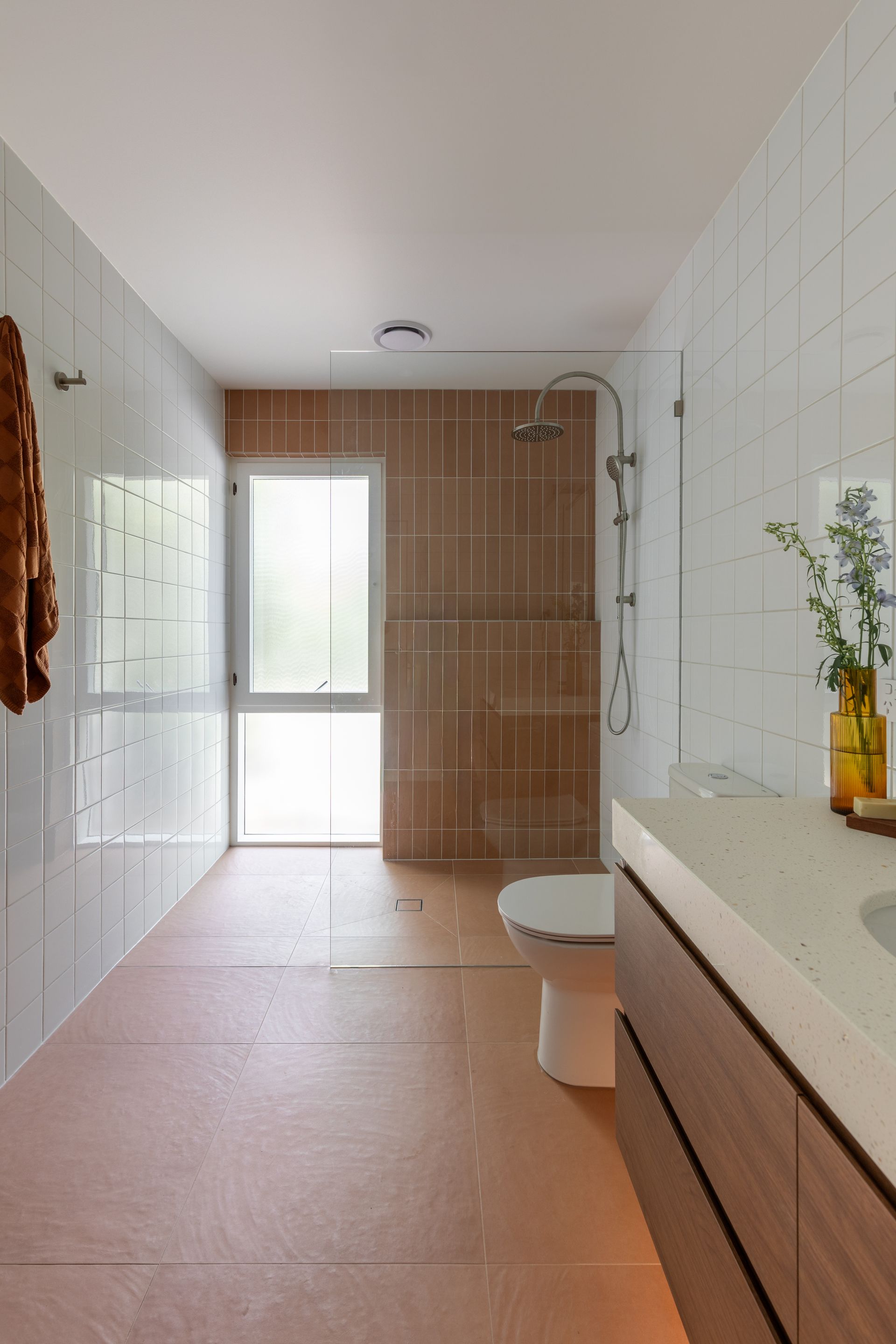 Modern bathroom with white tiled walls, beige floor, glass shower, toilet, and wood vanity.