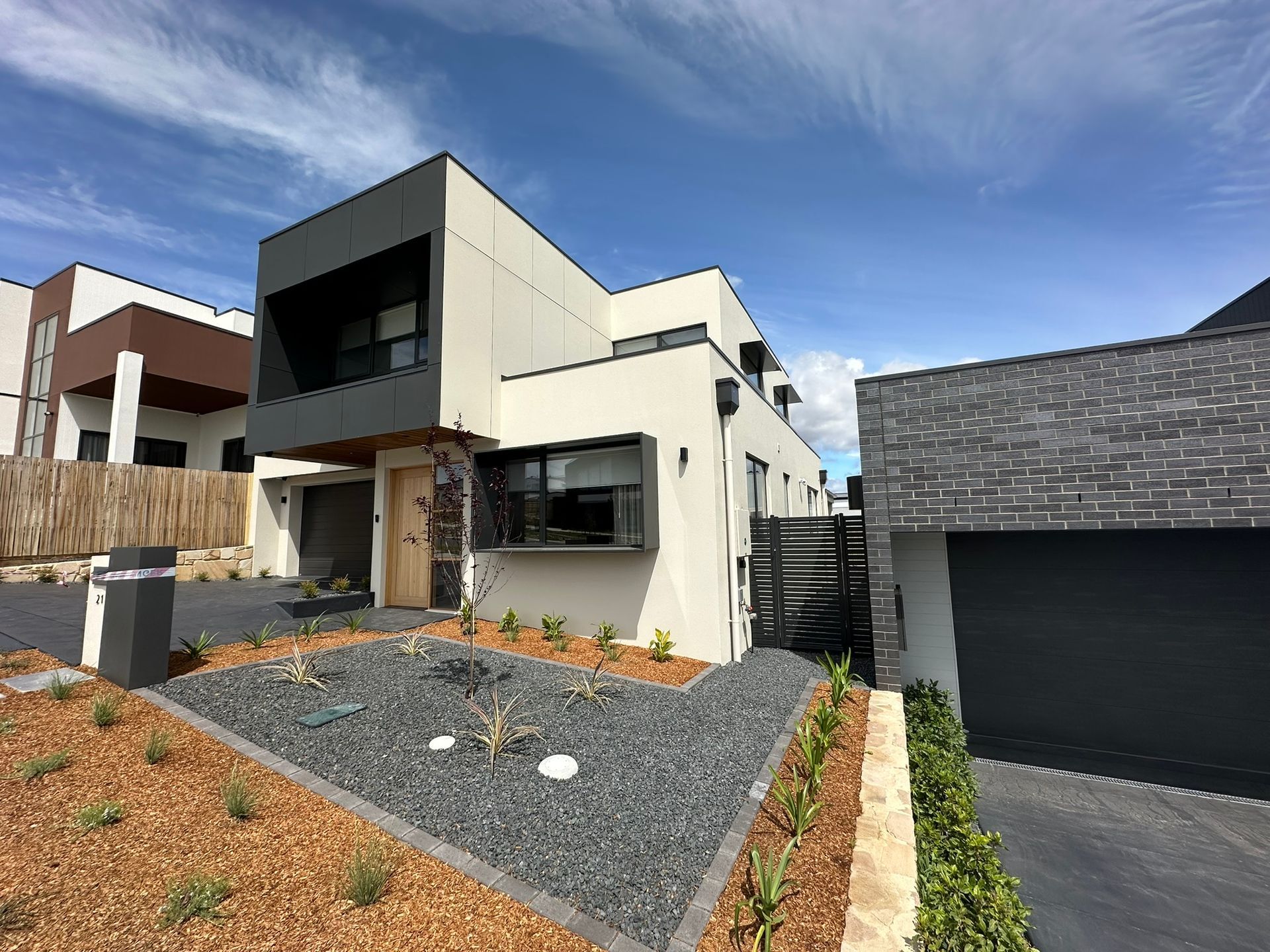 Modern two-story house with dark garage, gravel landscaping, and blue sky