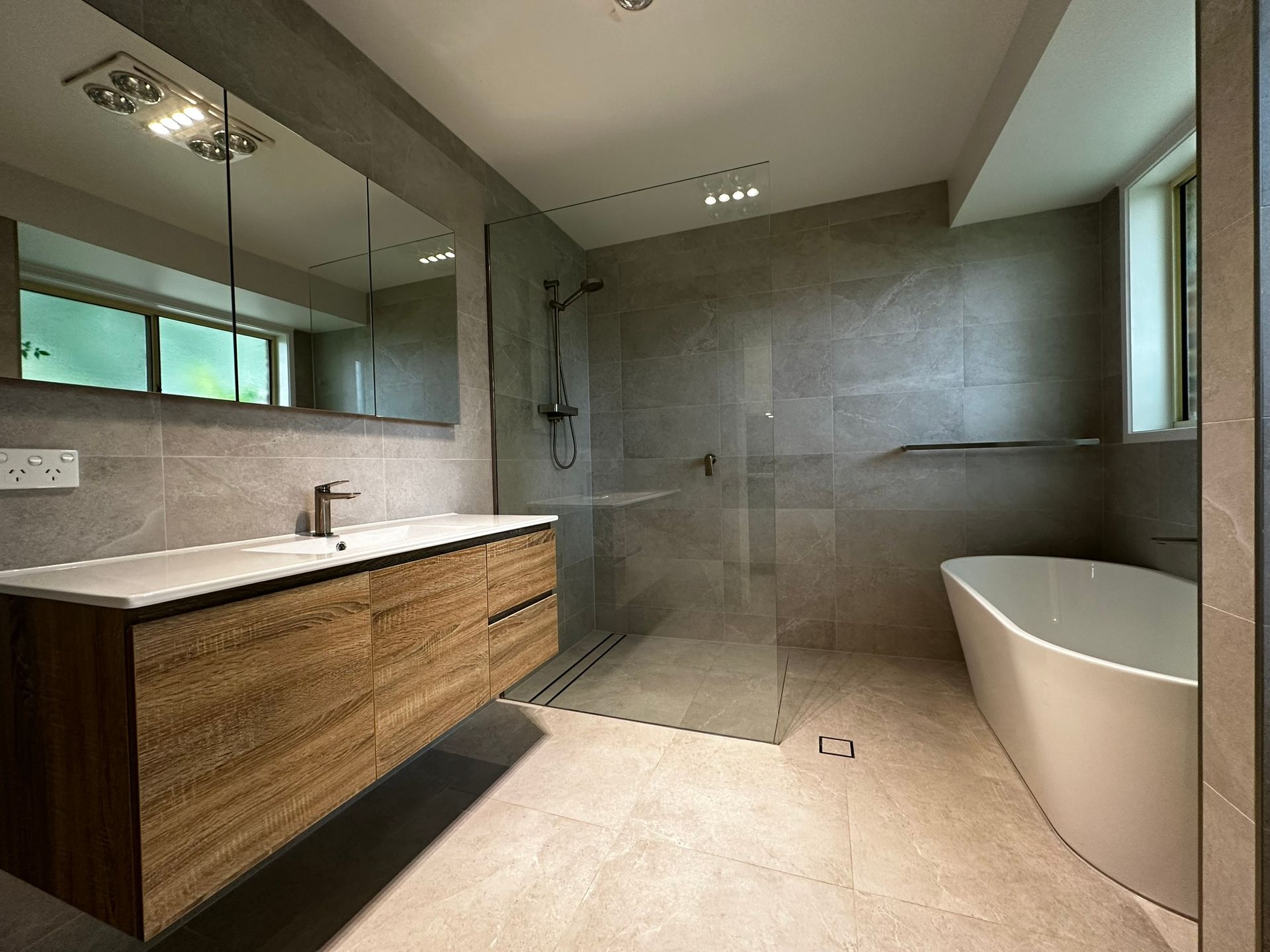 Modern bathroom with double vanity, large mirror, tiled shower, and freestanding bathtub