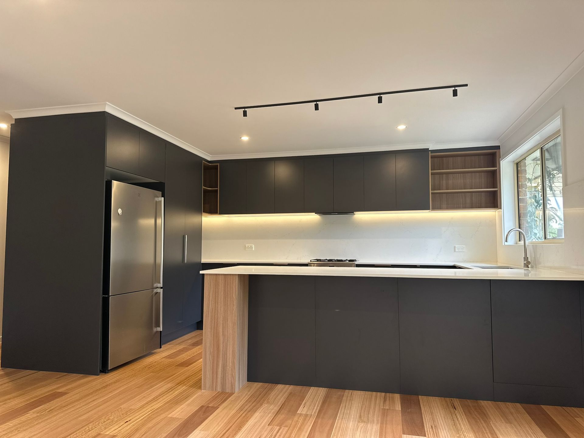 Modern black-and-white kitchen with wood floors, island, stainless fridge, and track lighting