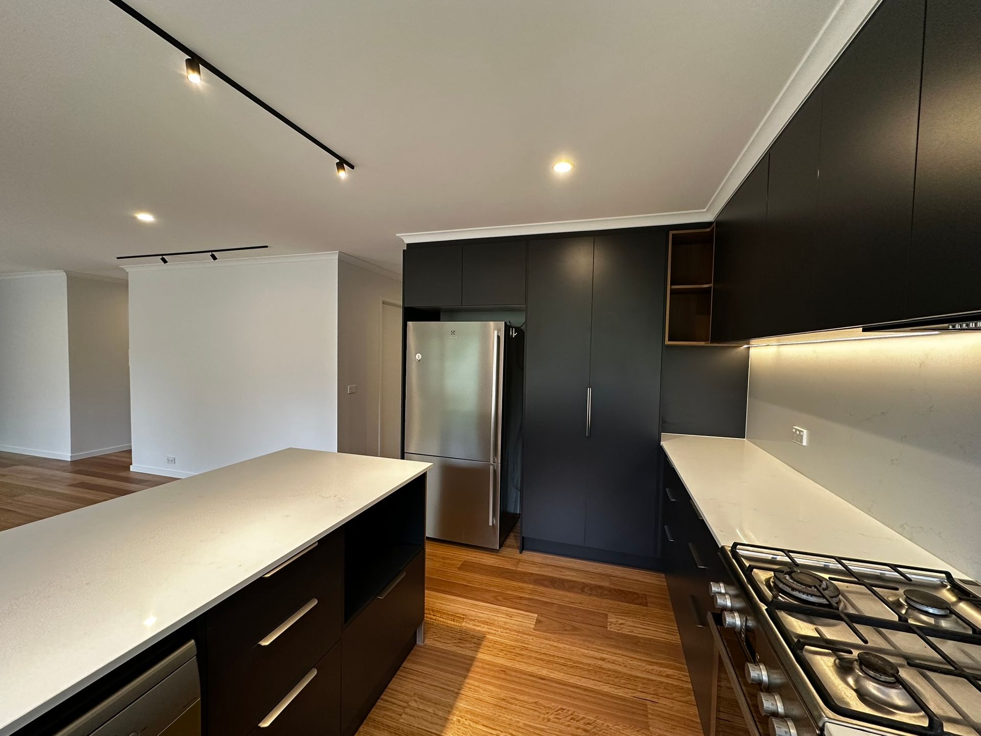 Modern kitchen with black cabinets, white countertops, wood floor, and stainless steel refrigerator.