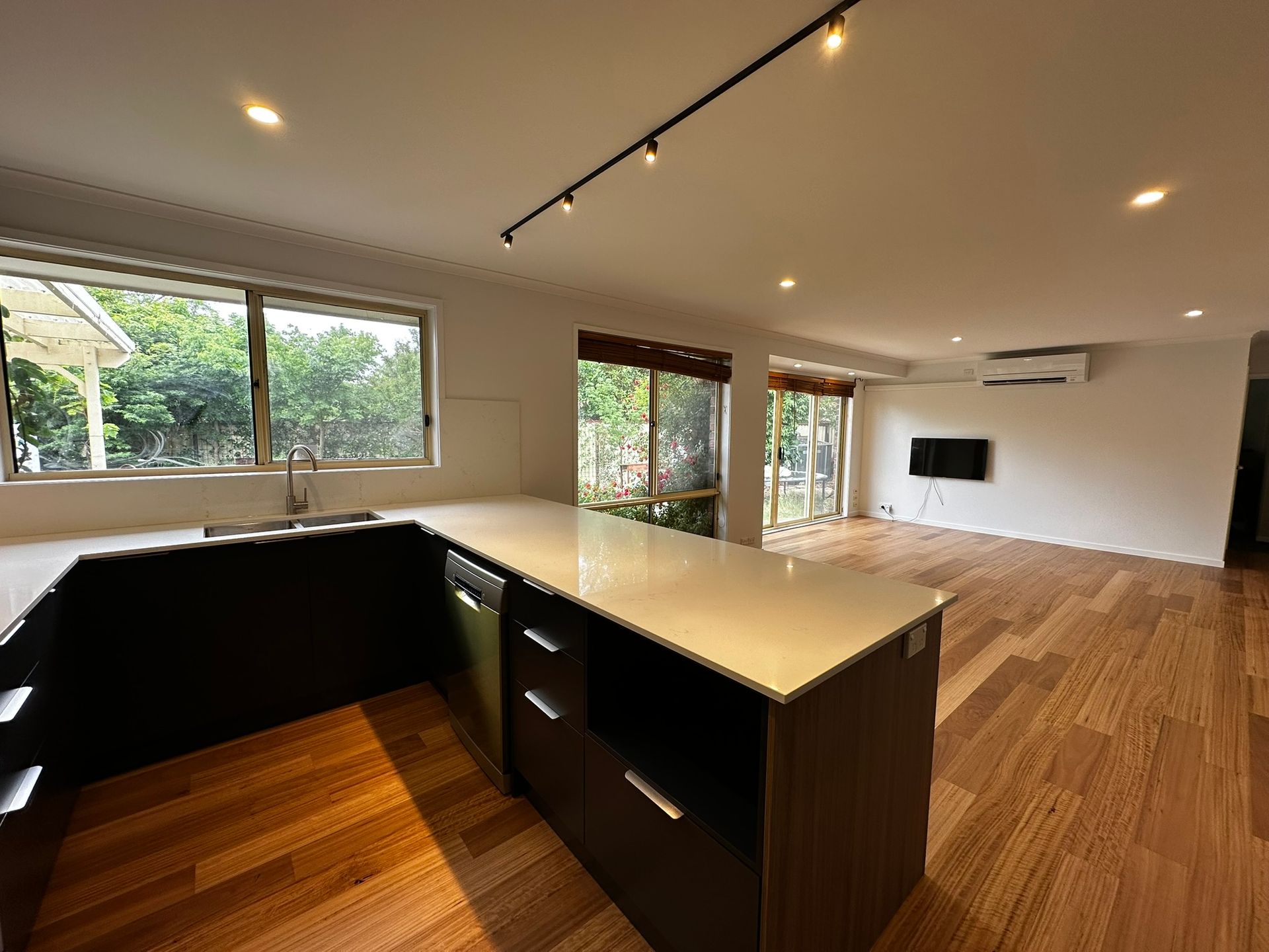 Modern open-plan kitchen and living room with wood floors, black island, large windows, and a wall-mounted TV