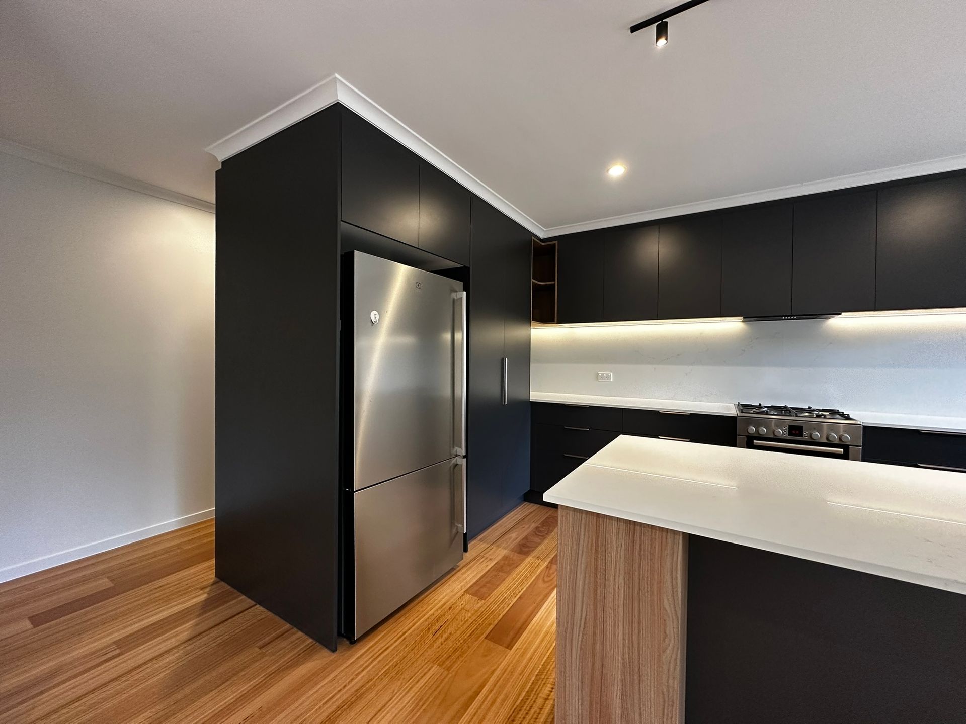 Modern kitchen with black cabinets, stainless steel fridge, white island, and wood flooring