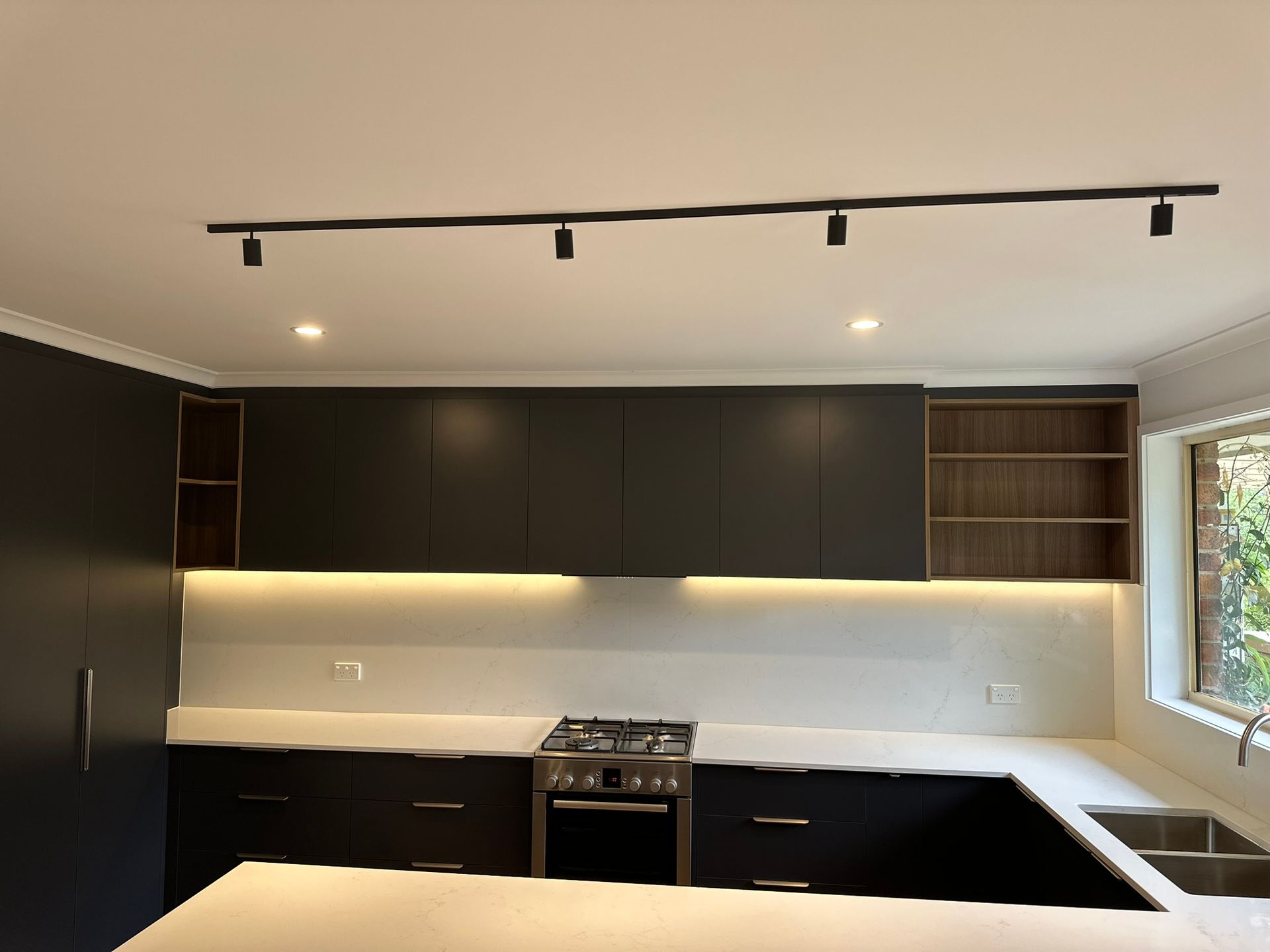 Modern kitchen with dark cabinets, white countertops, under-cabinet lighting, and a gas stove.