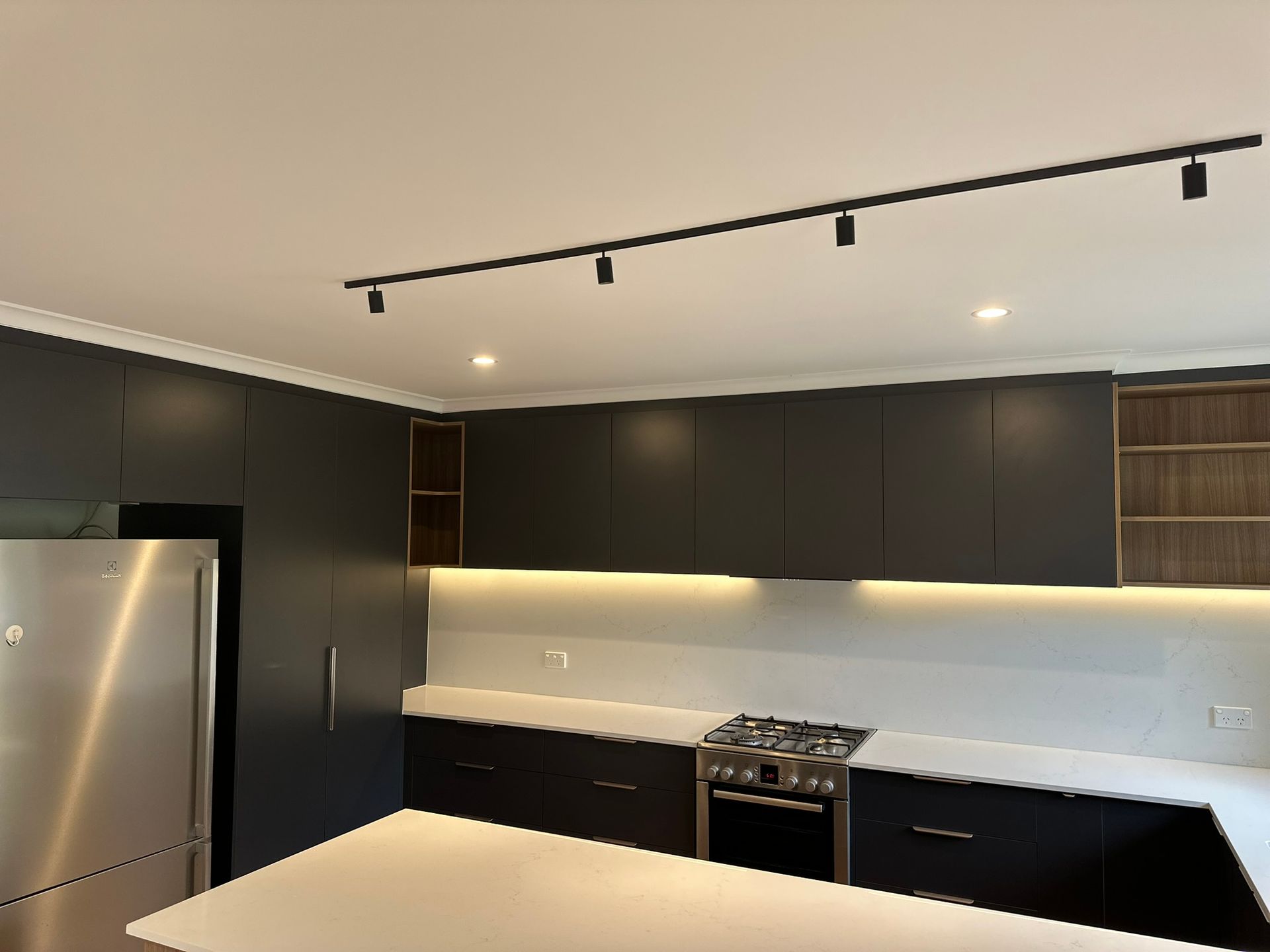 Modern kitchen with dark cabinets, stainless fridge, white countertops, and ceiling track lighting.