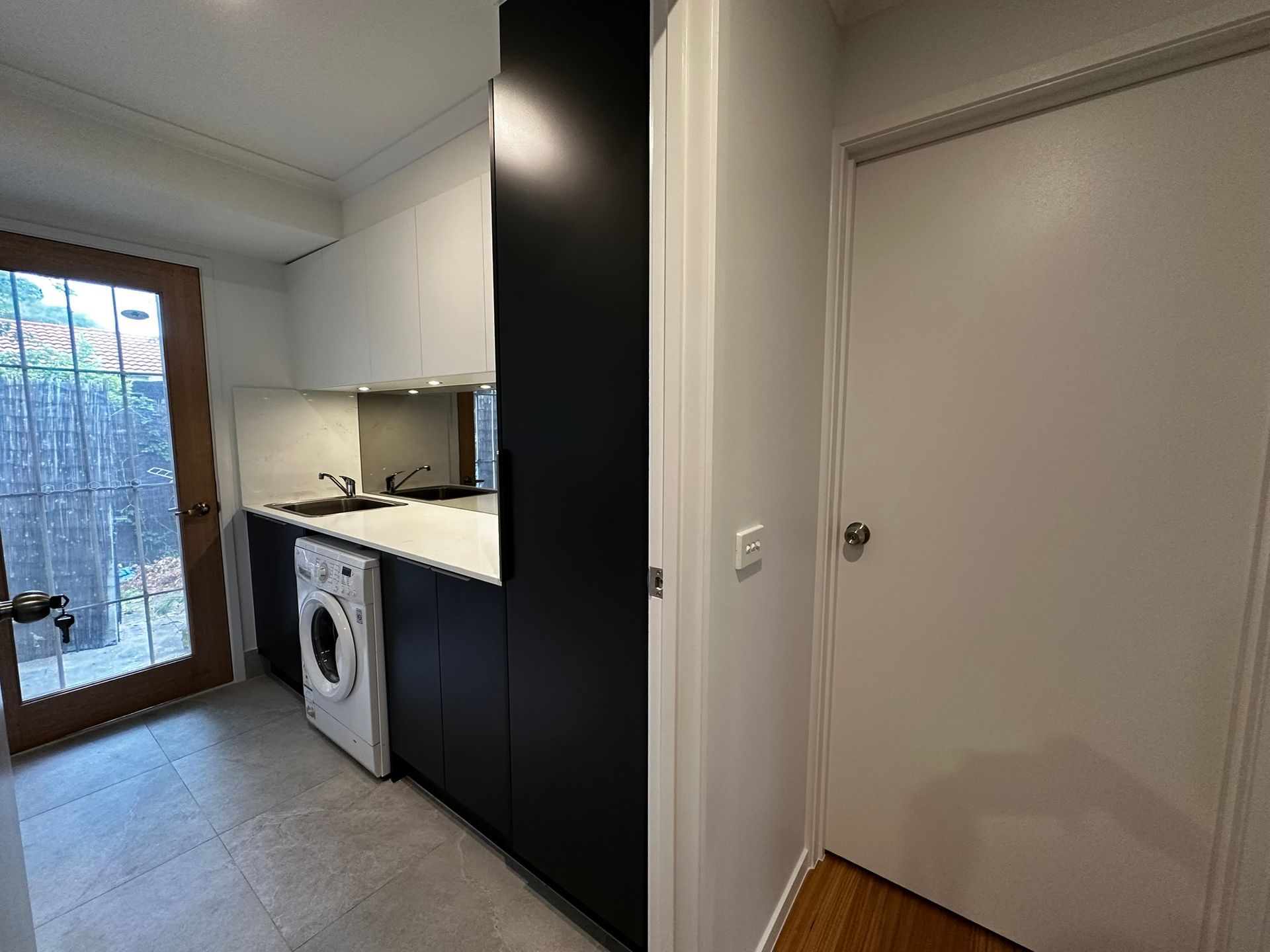 Small modern kitchen with white cabinets, dark lower cabinets, washer, and a glass door to a balcony.