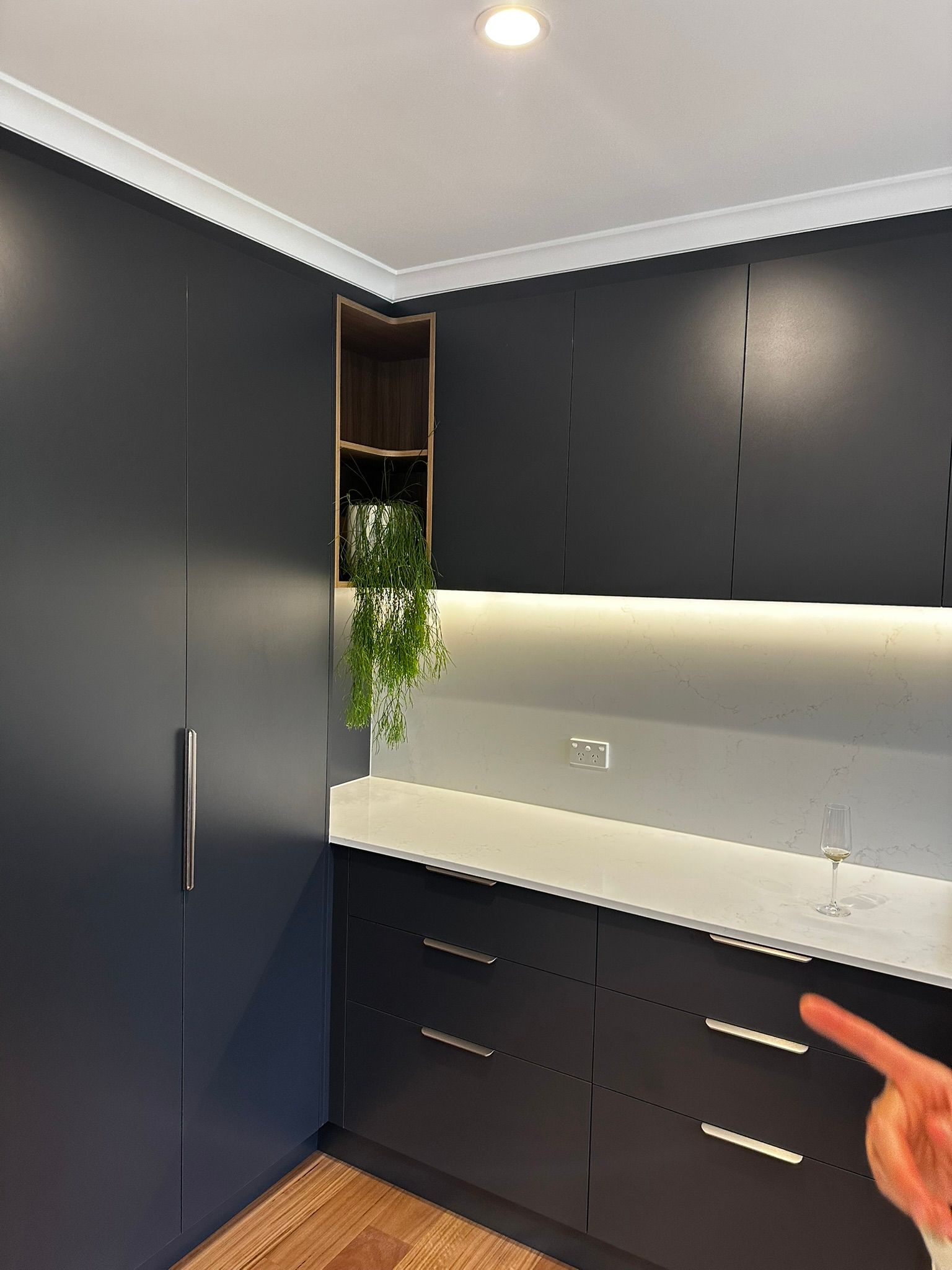 Modern kitchen with dark cabinets, white countertop, under-cabinet lighting, and a hand pointing at the drawers