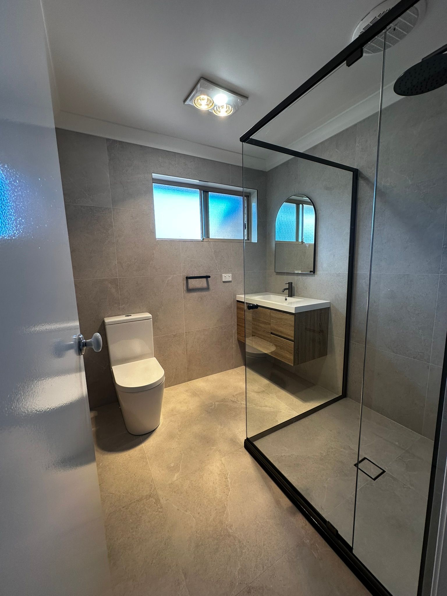 Modern bathroom with glass shower, sink vanity, toilet, and frosted windows