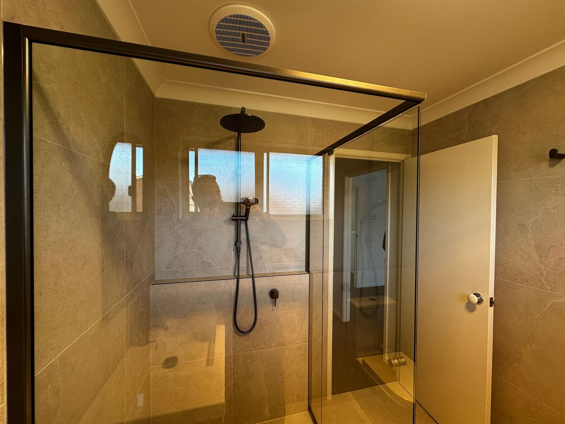 Modern bathroom shower with glass enclosure, beige tile walls, and a ceiling vent