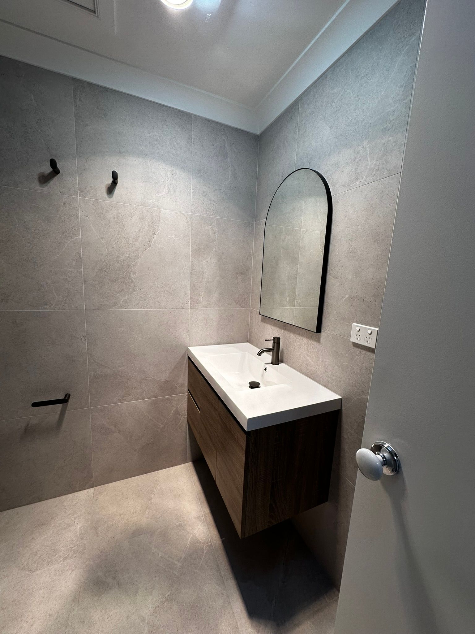 Modern gray bathroom with floating wood vanity, white sink, and arched mirror