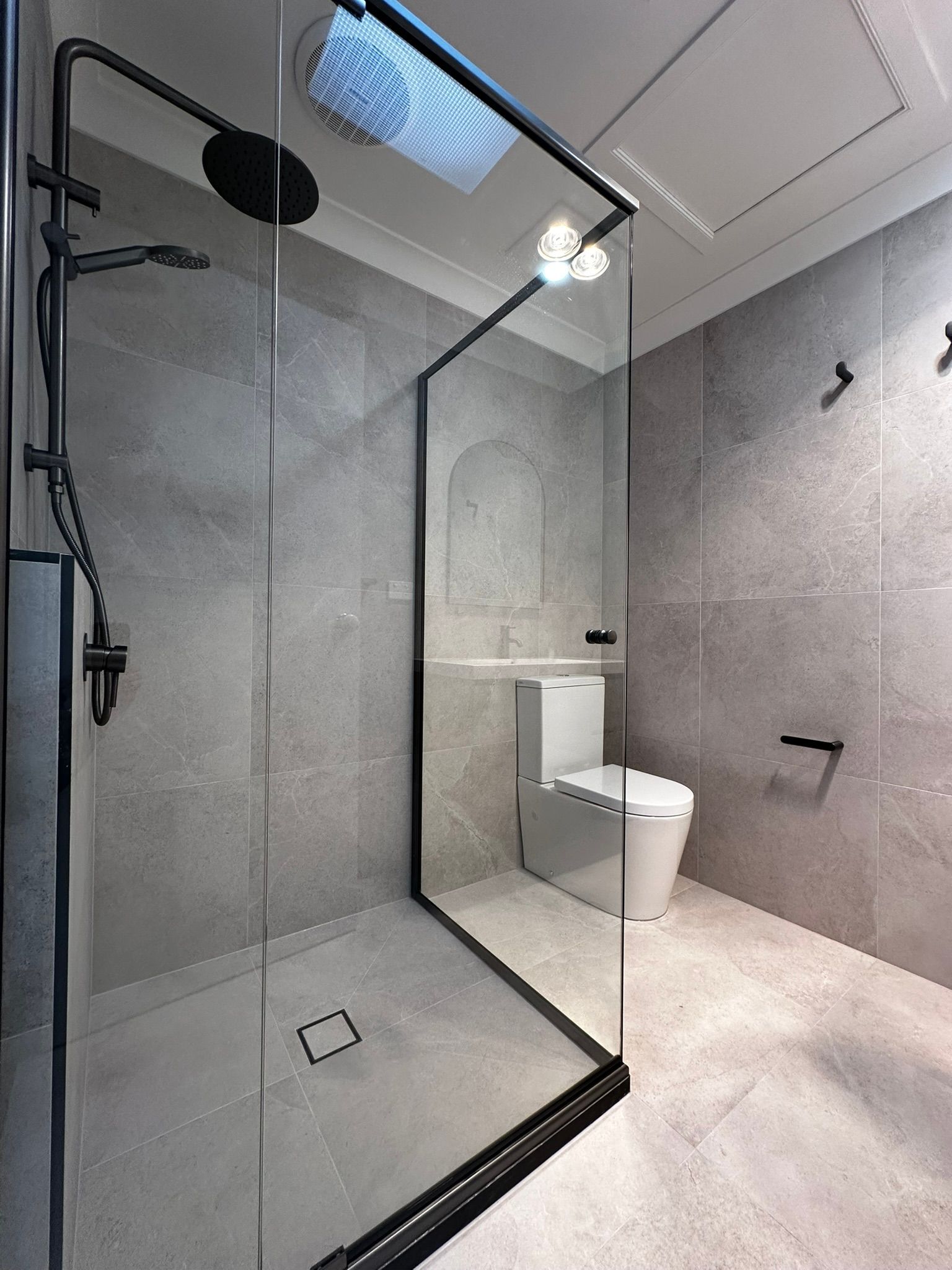 Modern gray bathroom with glass shower enclosure and white toilet under a skylight