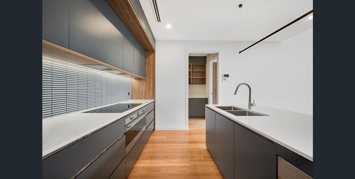 Modern kitchen with dark cabinets, white countertops, wood floor, and a large window splashback