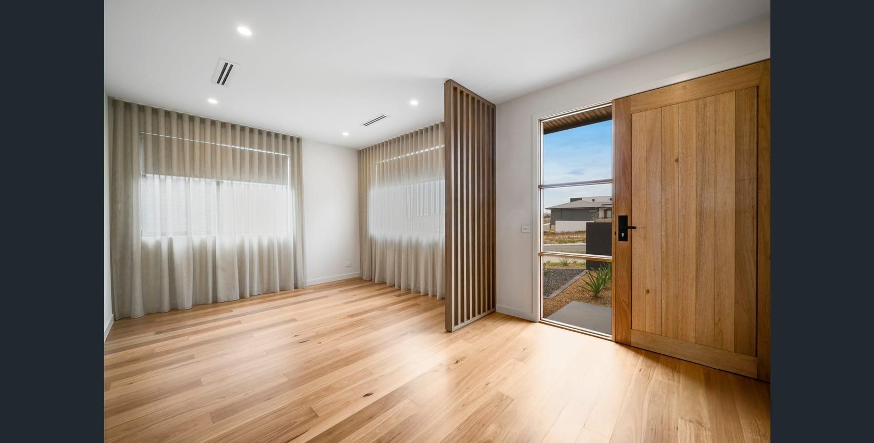 Empty modern living room with wood floors, white walls, and an open wooden door to a bright exterior.