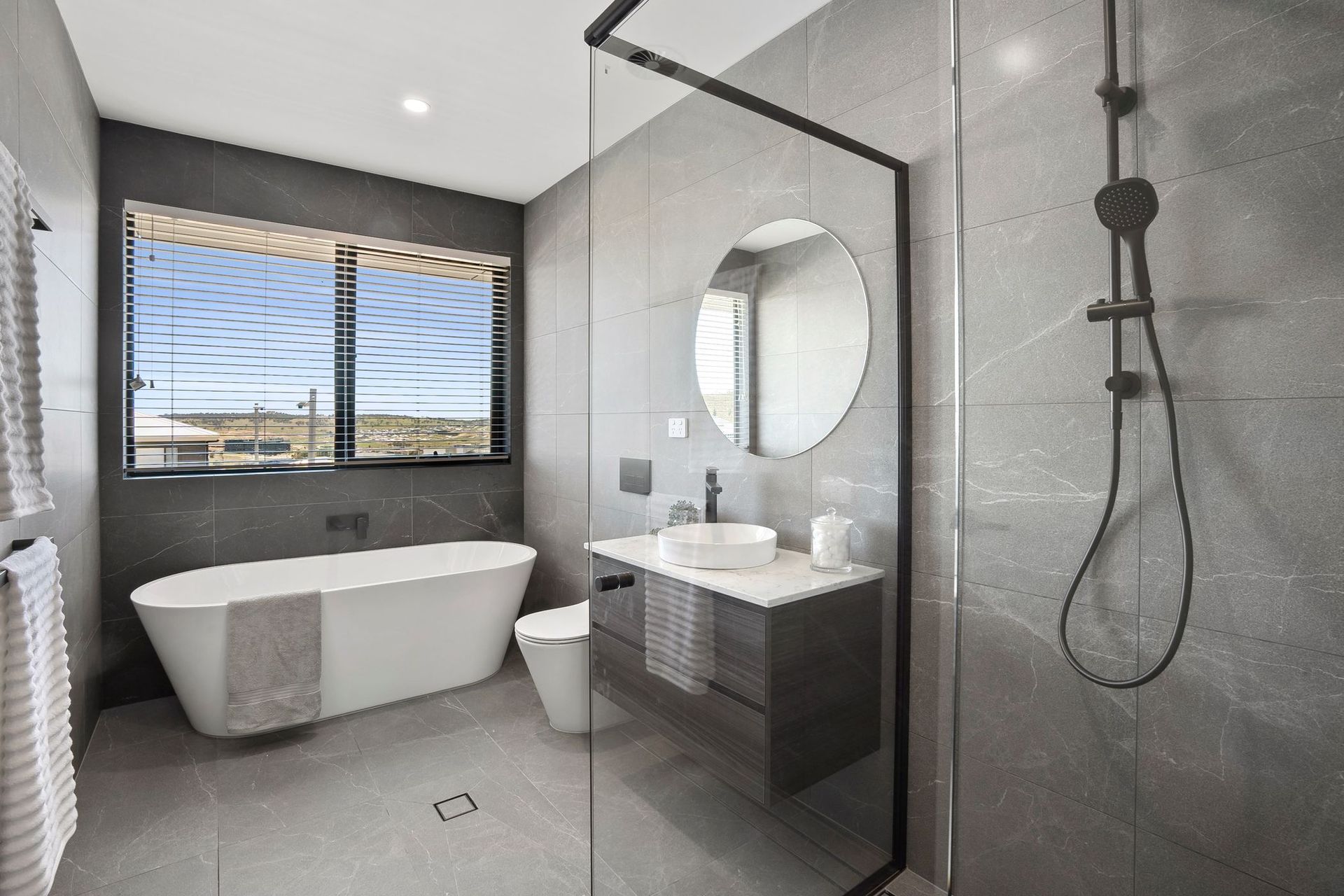 Modern gray bathroom with freestanding tub, walk-in shower, vanity, and window blinds
