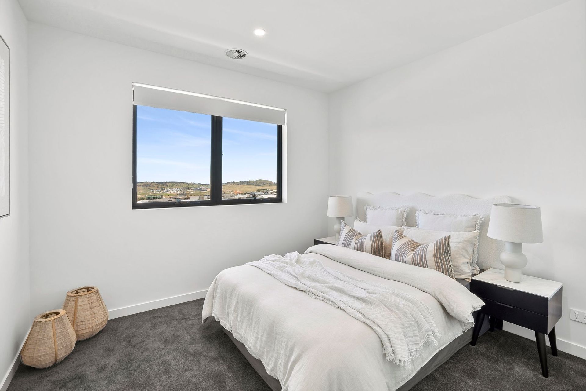 Bright bedroom with white bed, nightstand, window view, and gray carpet