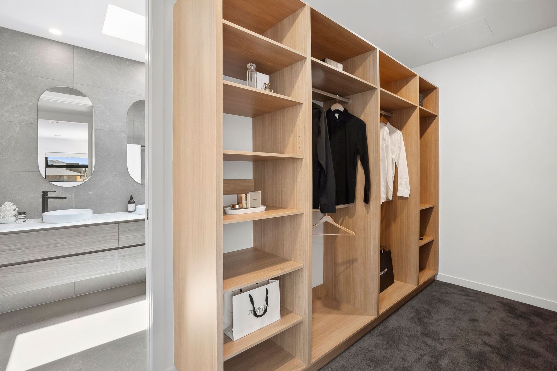 Modern walk-in closet with wood shelving, hanging clothes, and bathroom vanity visible beside it