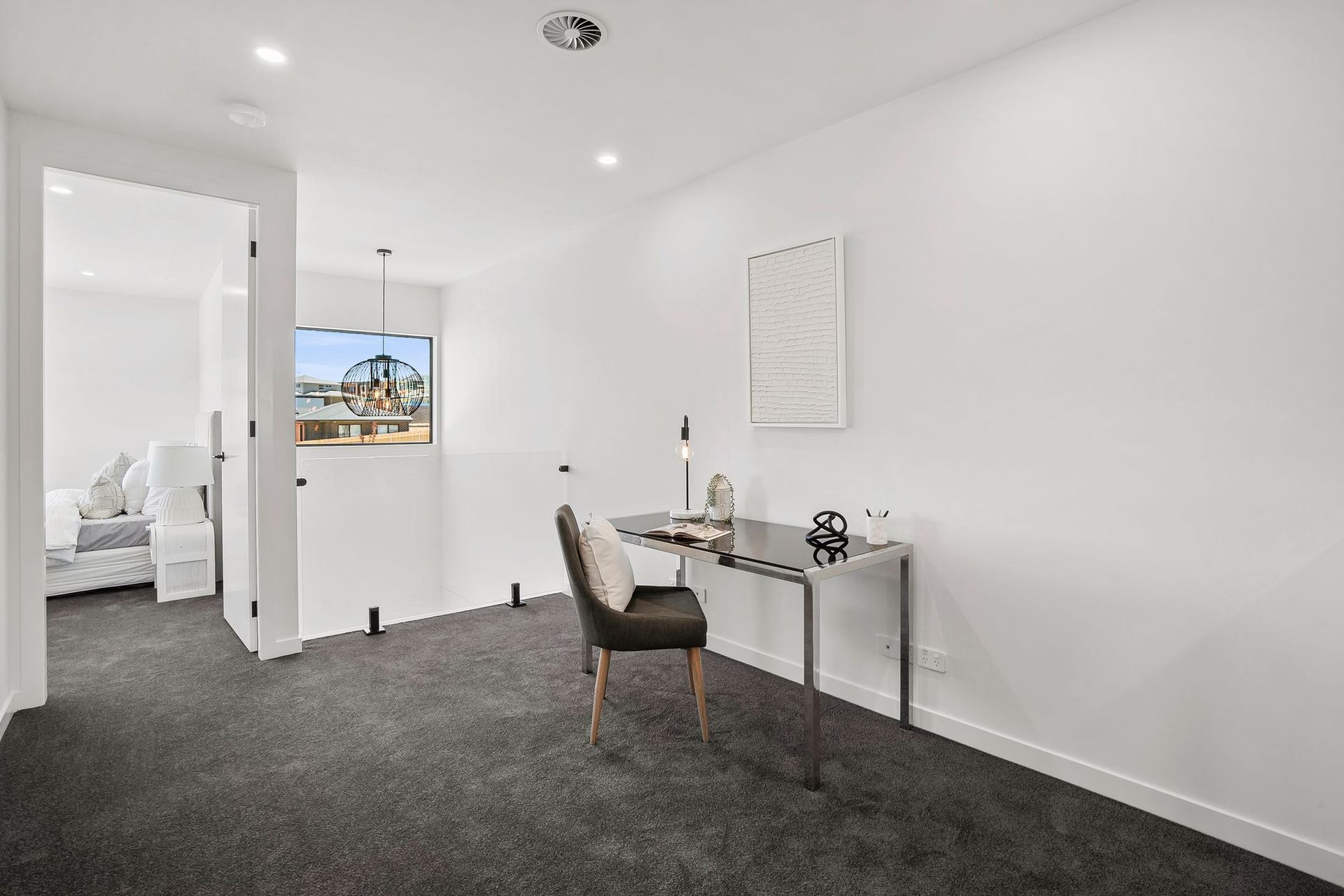 Bright empty white room with dark carpet, small desk and chair, and a view through an open doorway.