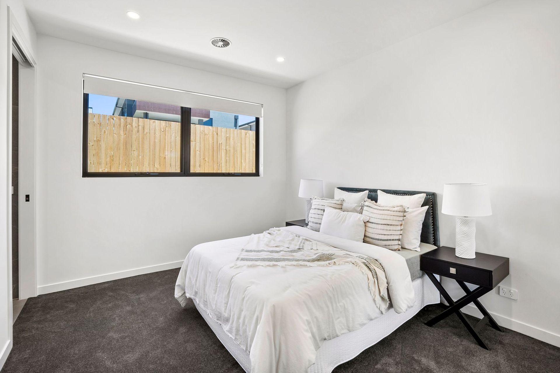 Bright minimalist bedroom with white bedding, dark carpet, and a window letting in natural light