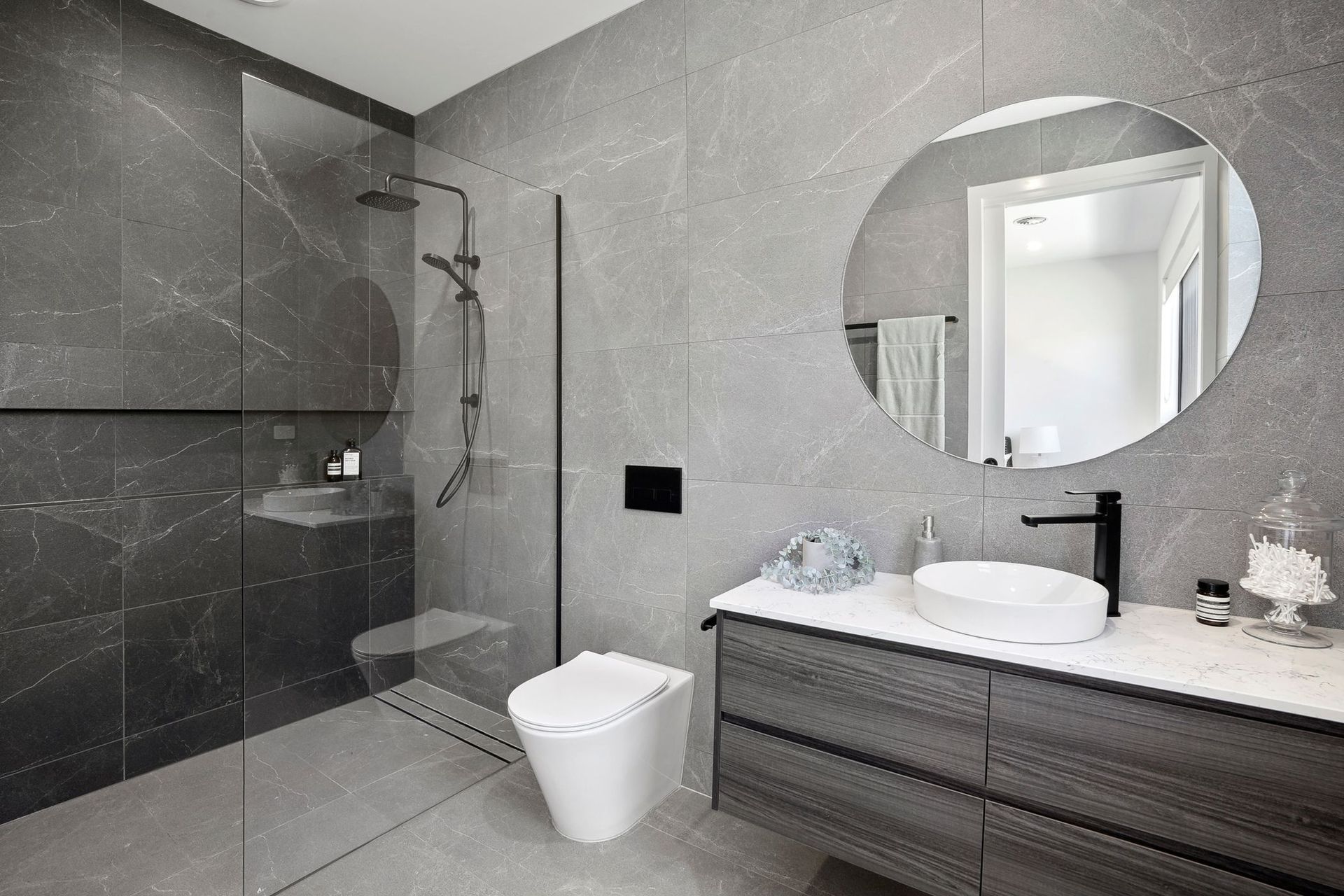Modern gray bathroom with walk-in shower, toilet, and vanity with round mirror.