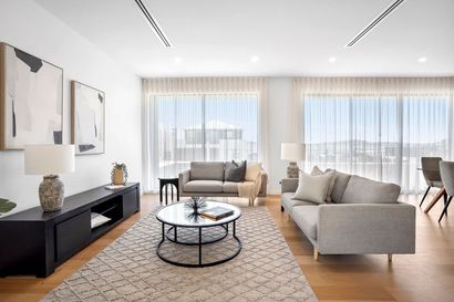 Bright modern living room with beige sofas, round coffee table, rug, TV console, and large windows