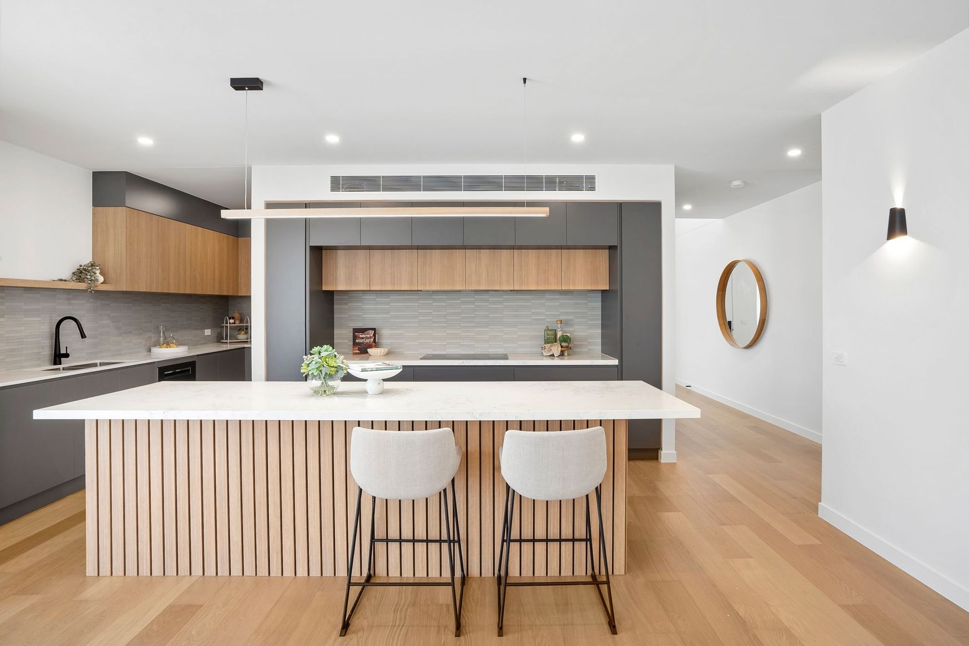 Modern kitchen with white island, wood cabinets, black countertops, and wood floors.