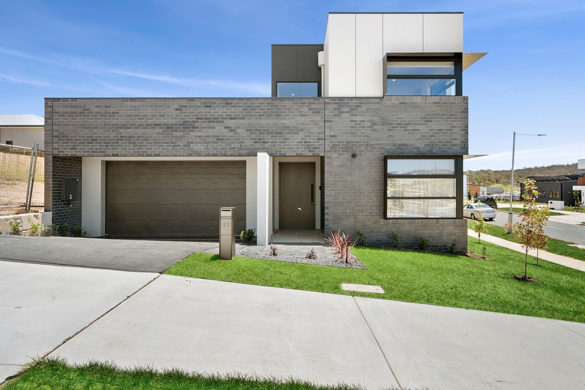 Modern two-story gray house with a garage, front lawn, and driveway under a clear sky