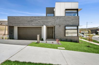 Modern two-story house with gray brick facade, garage, and front lawn under a blue sky
