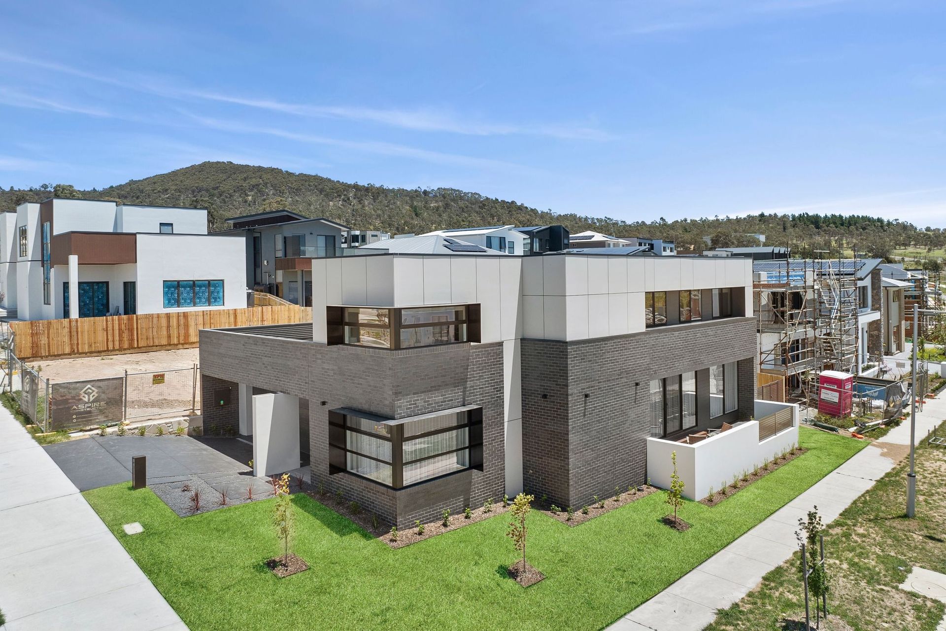 Modern townhouses with gray and white exteriors beside a grassy courtyard, with hills in the background