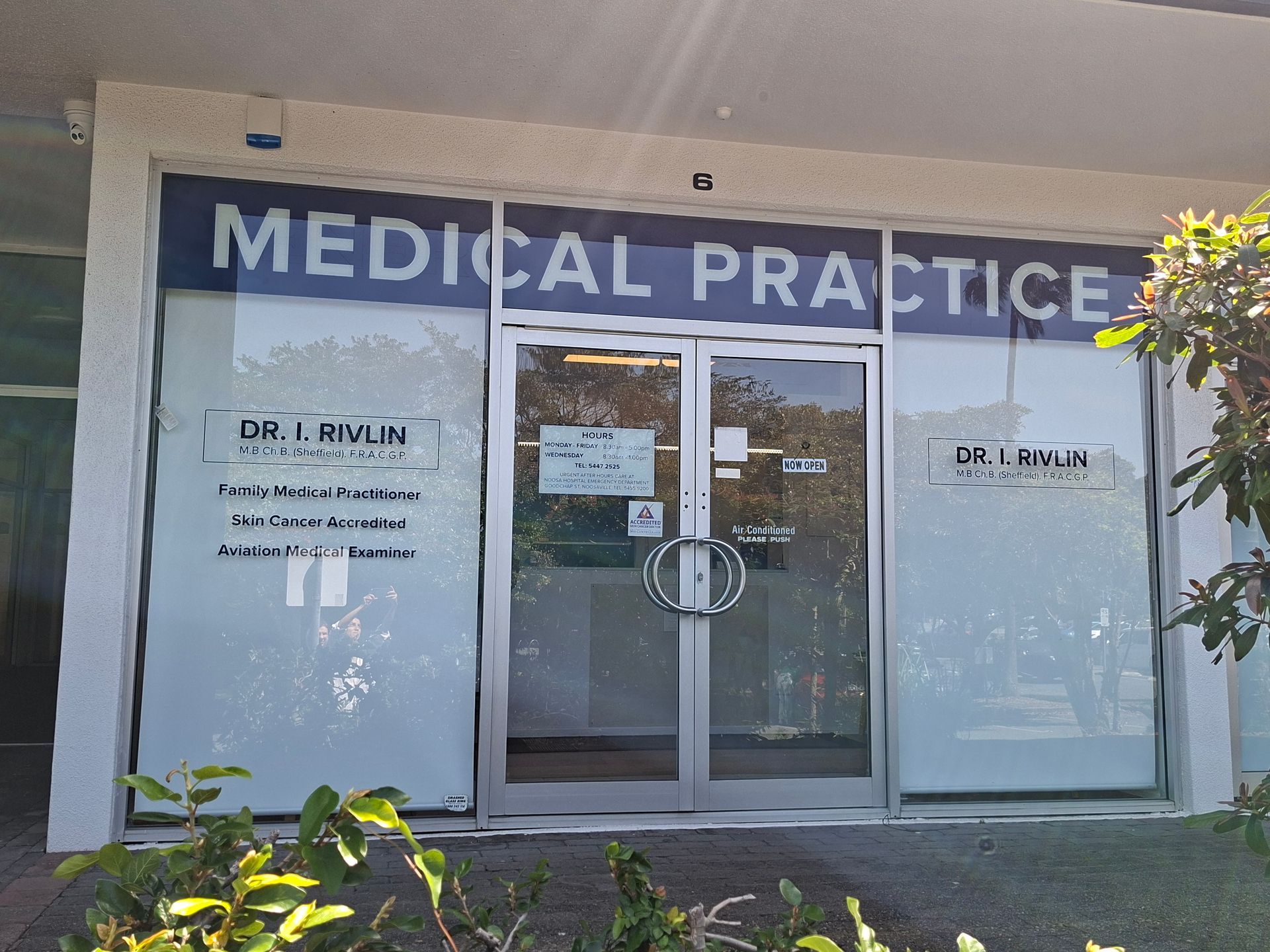Medical practice storefront with glass doors, white signage, and potted plants outside