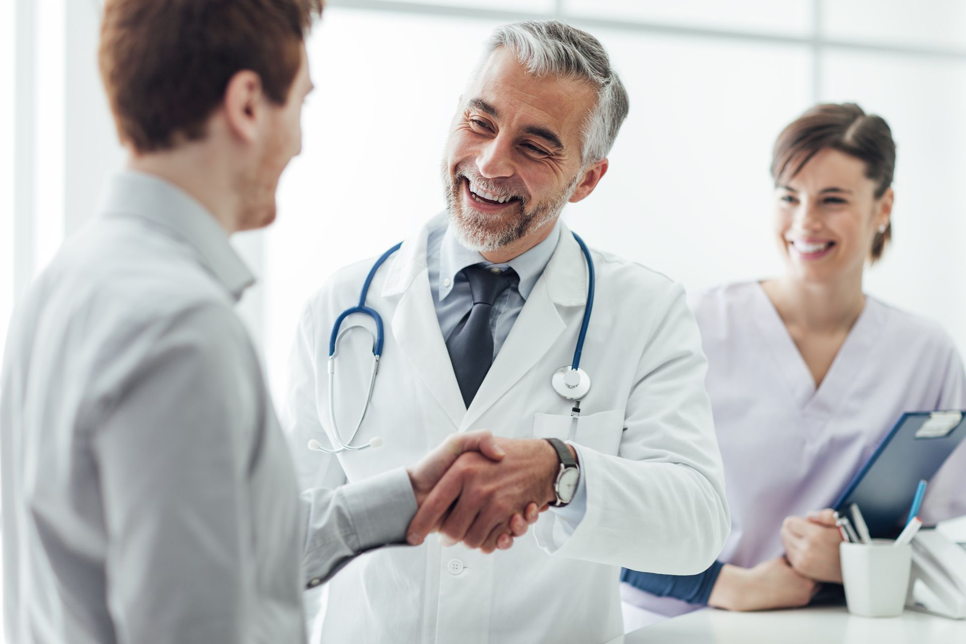 Doctor shaking hands with a patient in a bright clinic, with a smiling nurse in the background