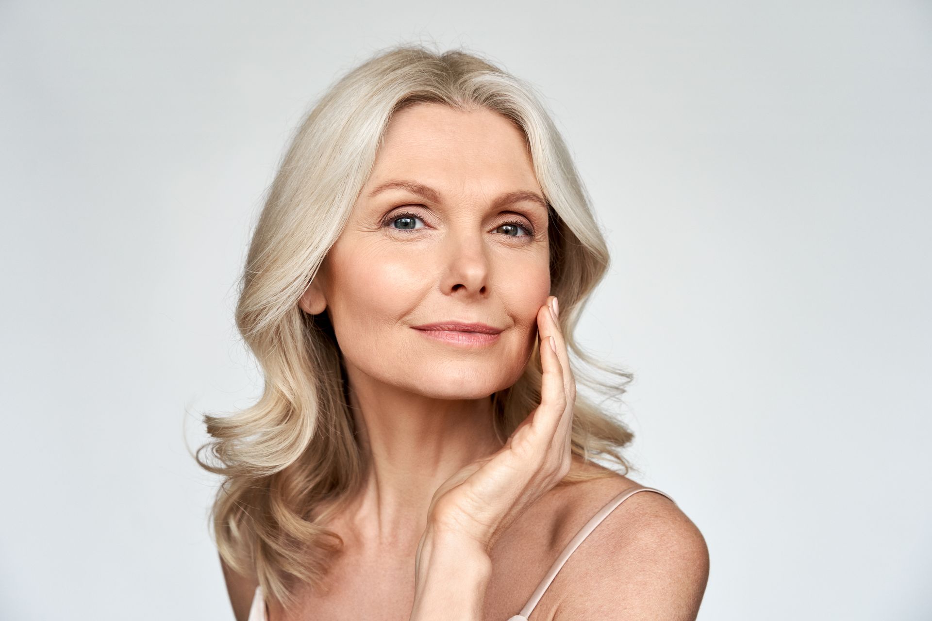 Portrait of a smiling woman with silver hair touching her face against a light background