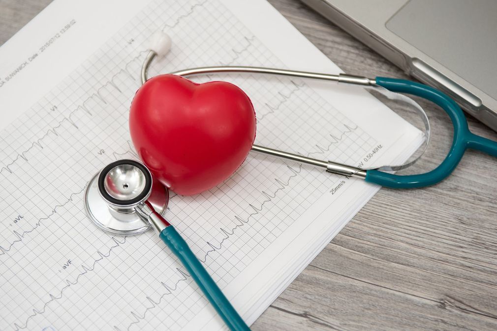 Red heart with stethoscope on medical chart beside a laptop, symbolizing healthcare or heart health