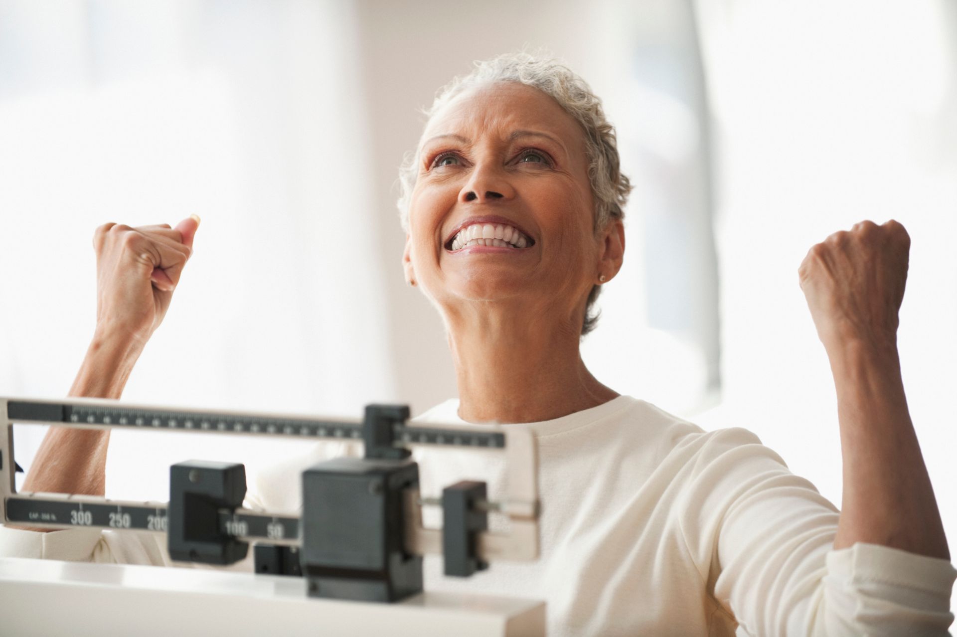 Person smiling and celebrating on a bathroom scale in a bright room