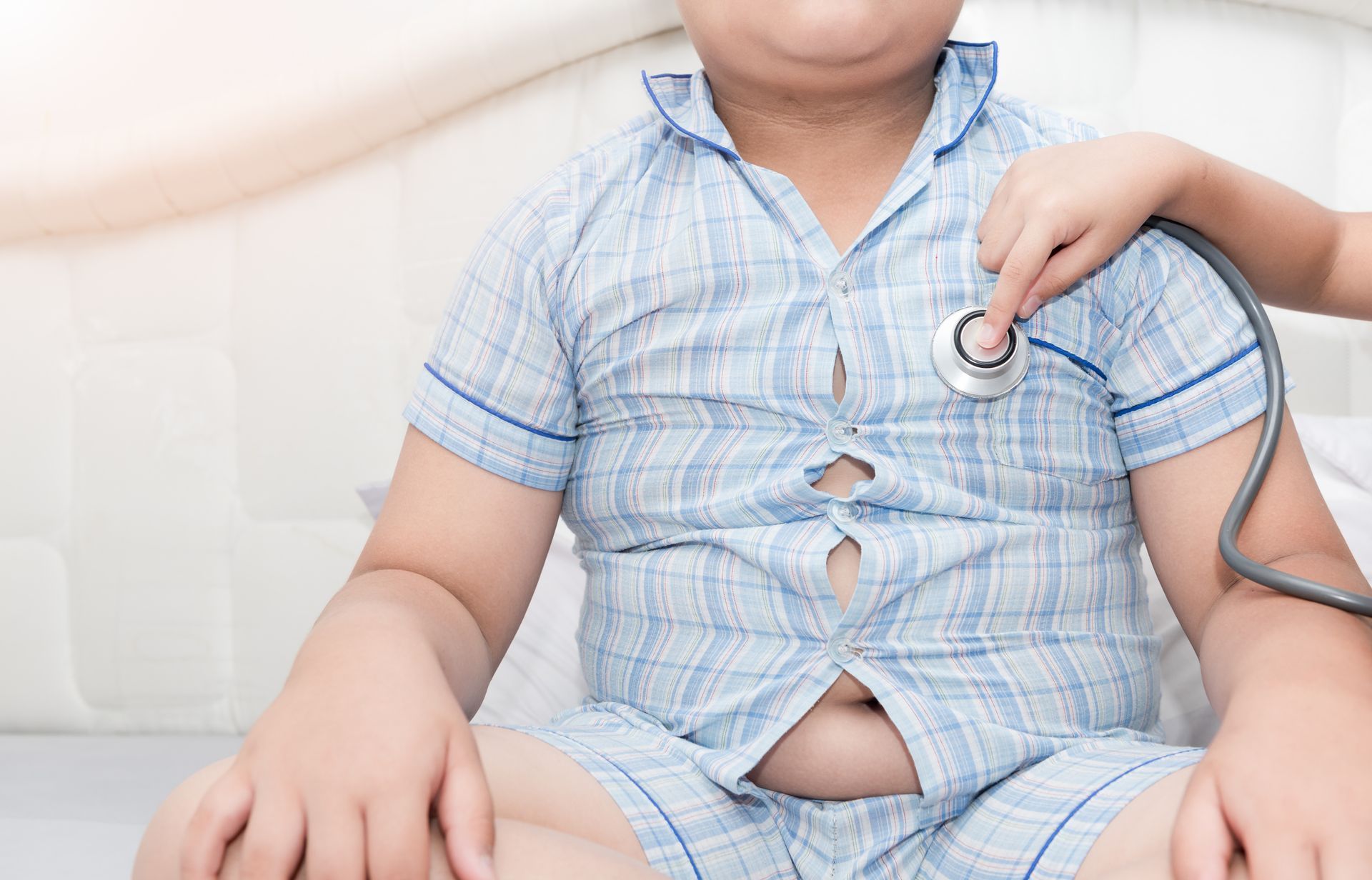 Child in blue checkered pajamas holding a stethoscope in a medical setting