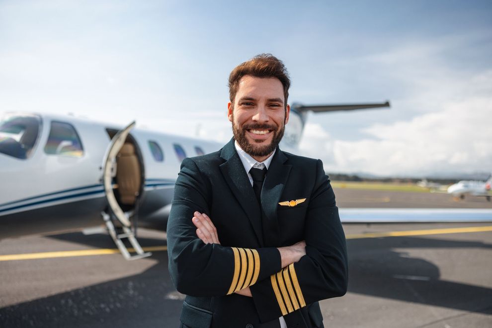 Pilot standing in front of a private jet with arms crossed, smiling on the tarmac.
